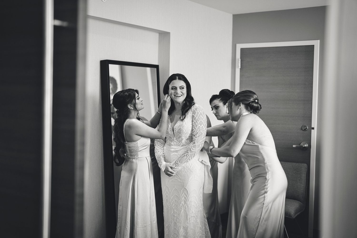 Black and white photo of bridesmaids helping with final wedding dress preparations in a room.