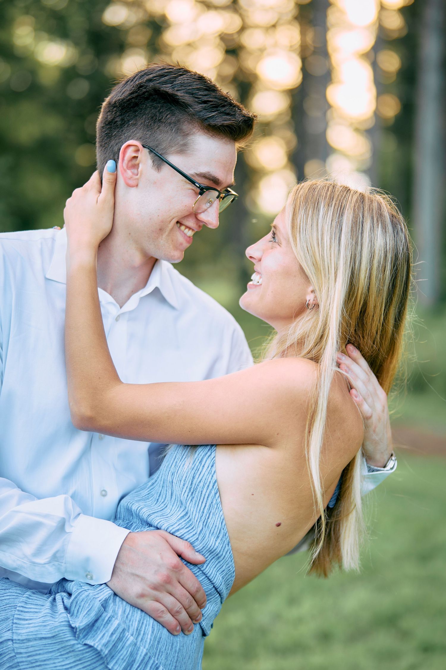 A romantic outdoor portrait of a couple embracing and smiling at each other in warm sunset lighting.