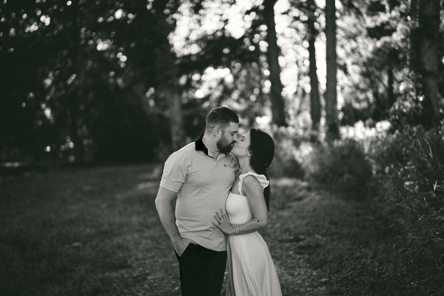 A romantic black and white photo of a couple embracing on a wooded path.