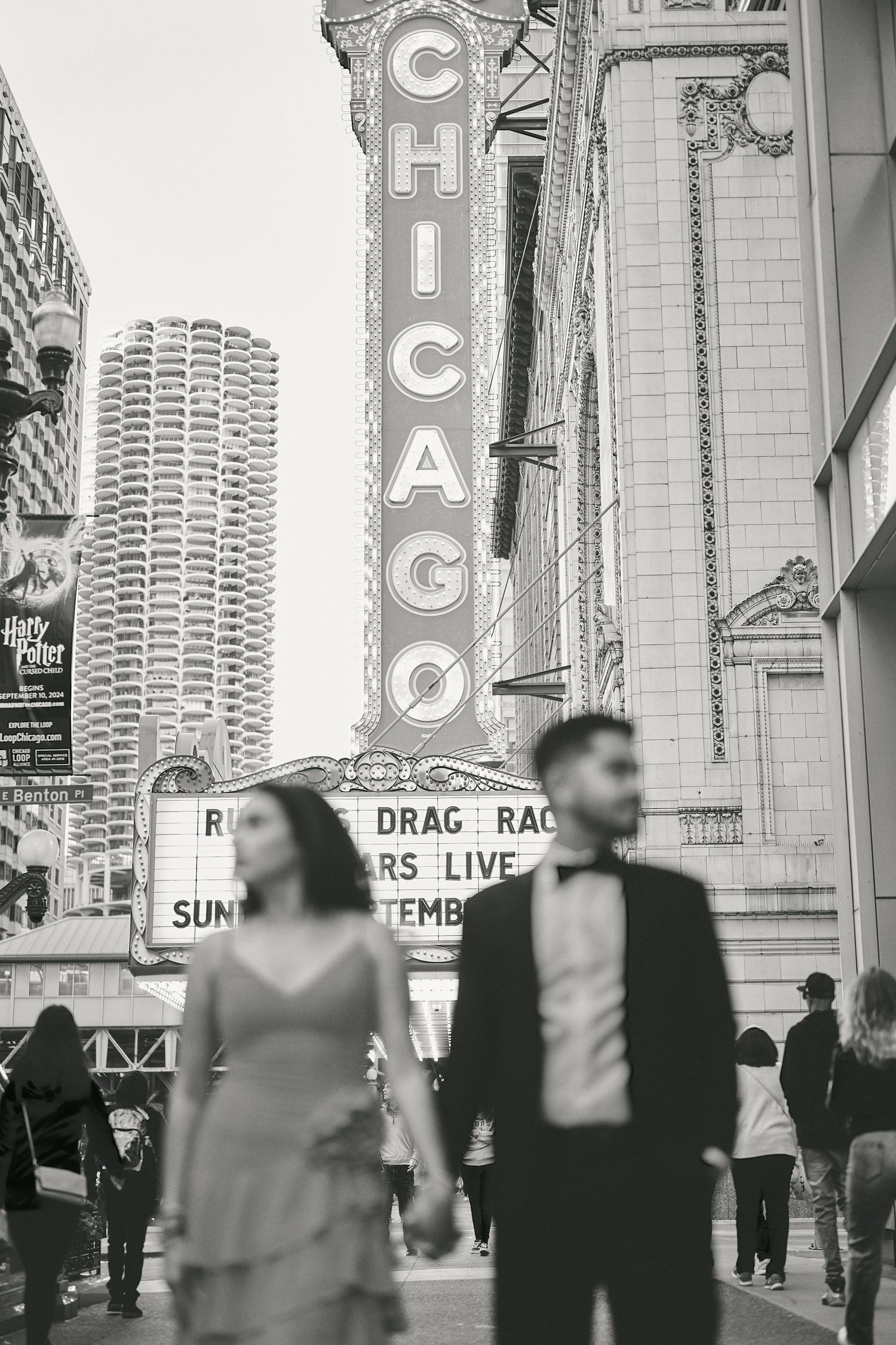 A black and white photo outside the iconic Chicago Theatre with its vertical marquee sign and crowds below.