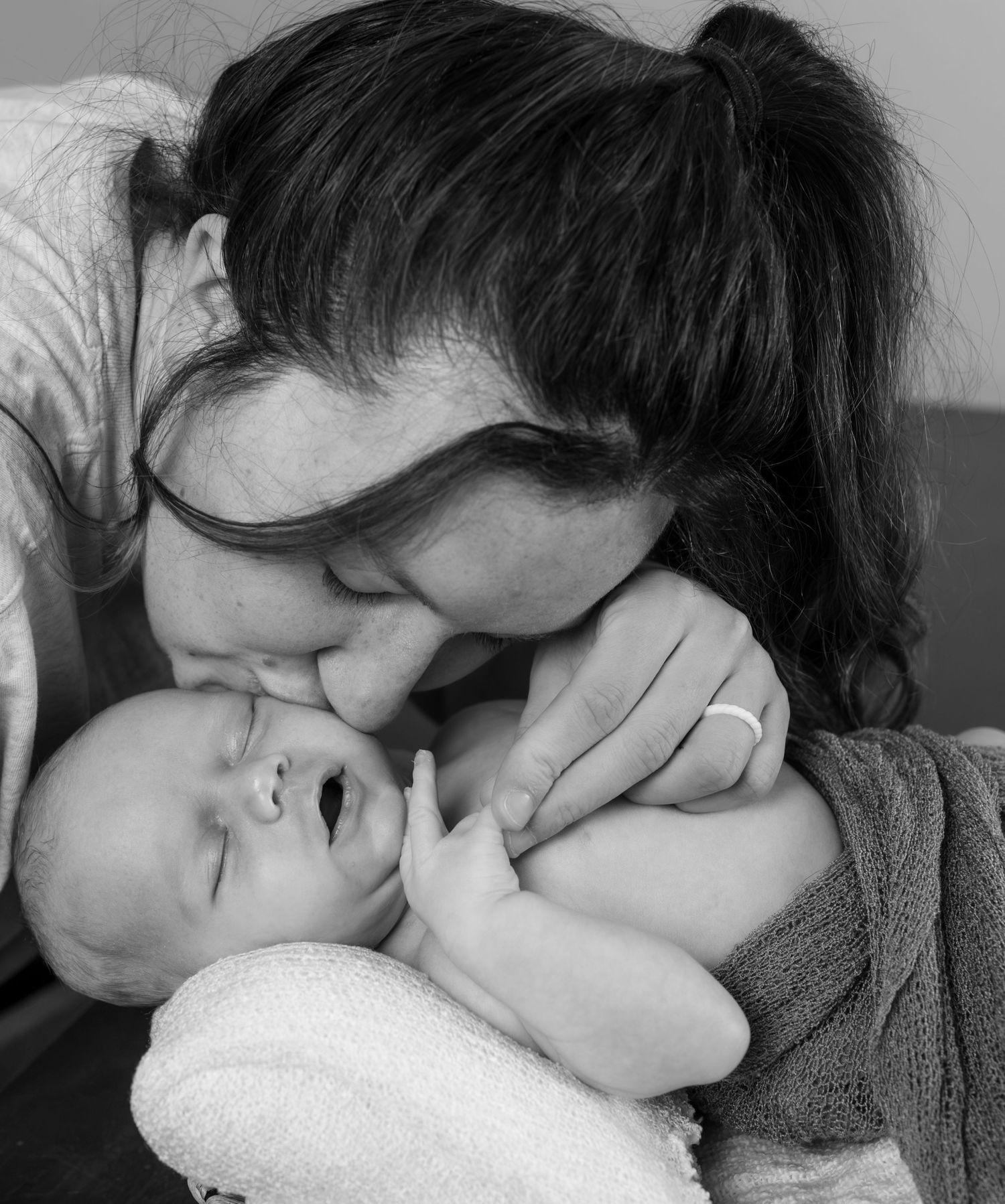 A new Mother kisses her newborns cheek in this in home newborn session.