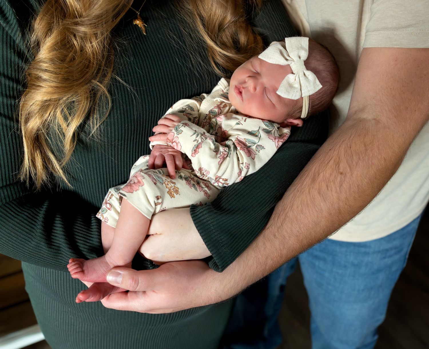 A newborn baby girl sleeps peacefully in her mom and dads arms