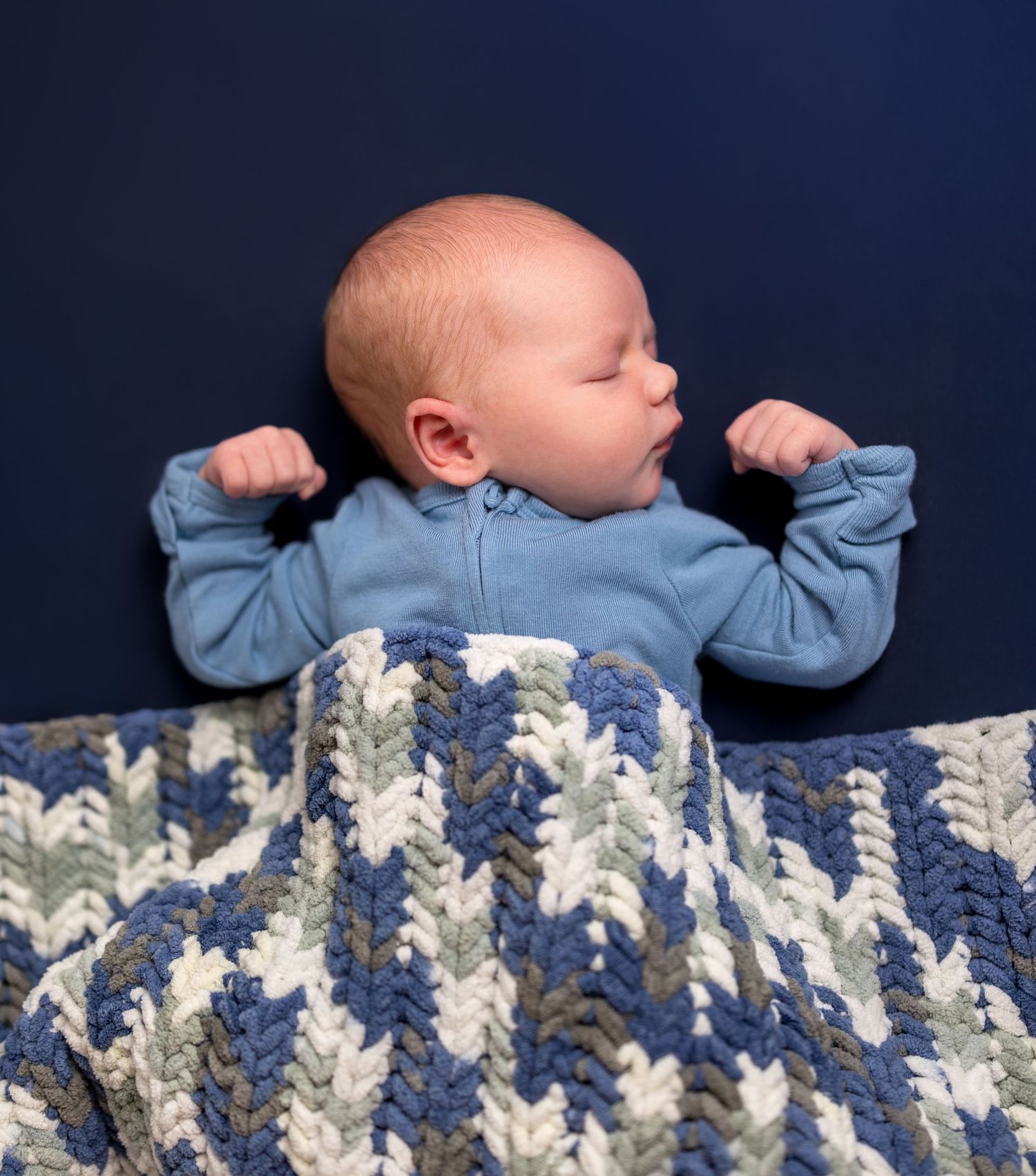 A newborn sleeps in his crib wrapped in a knit chevron blanket.