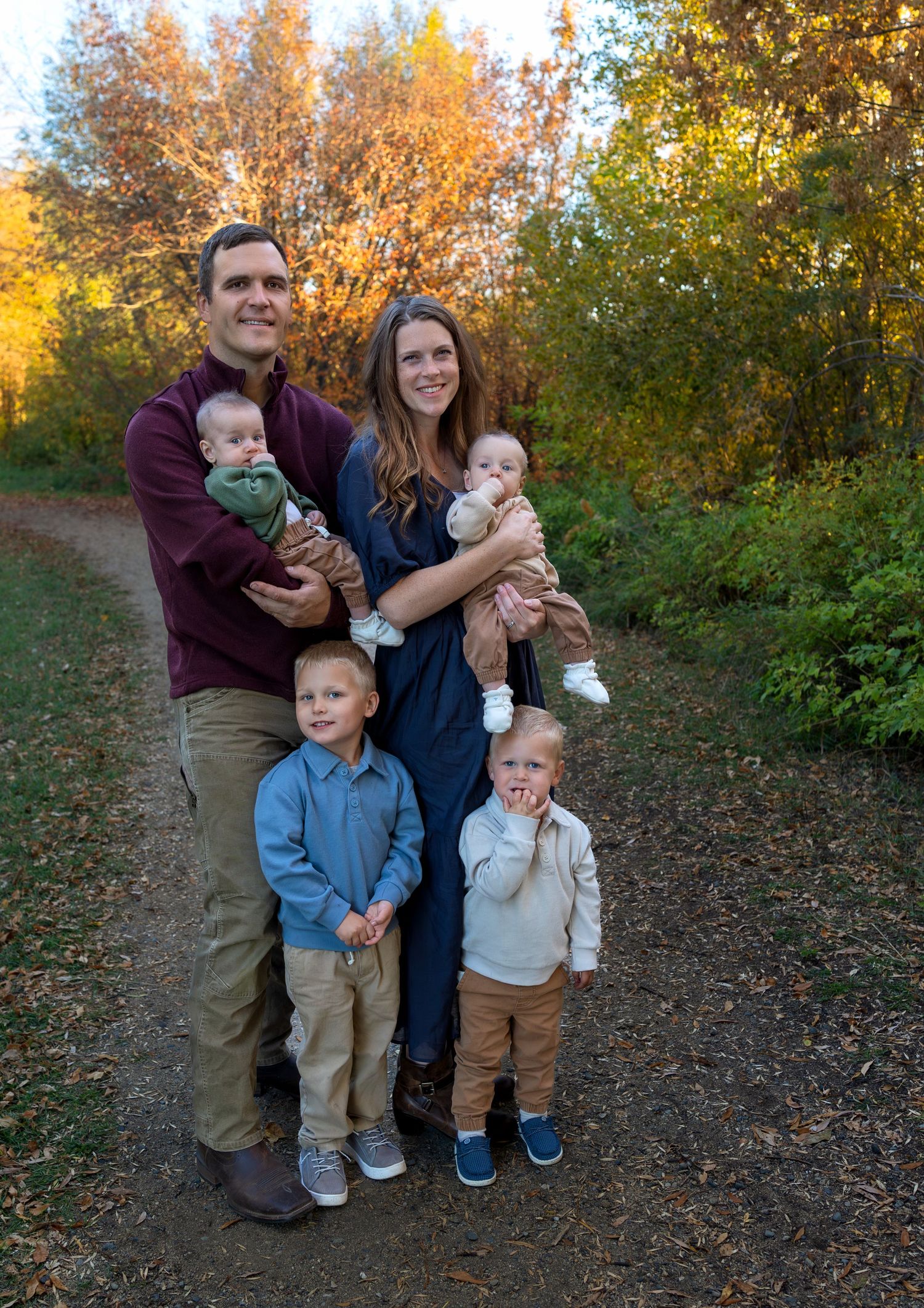 A family of six pose for autumn family photos with trees of orange, yellow and green behind them