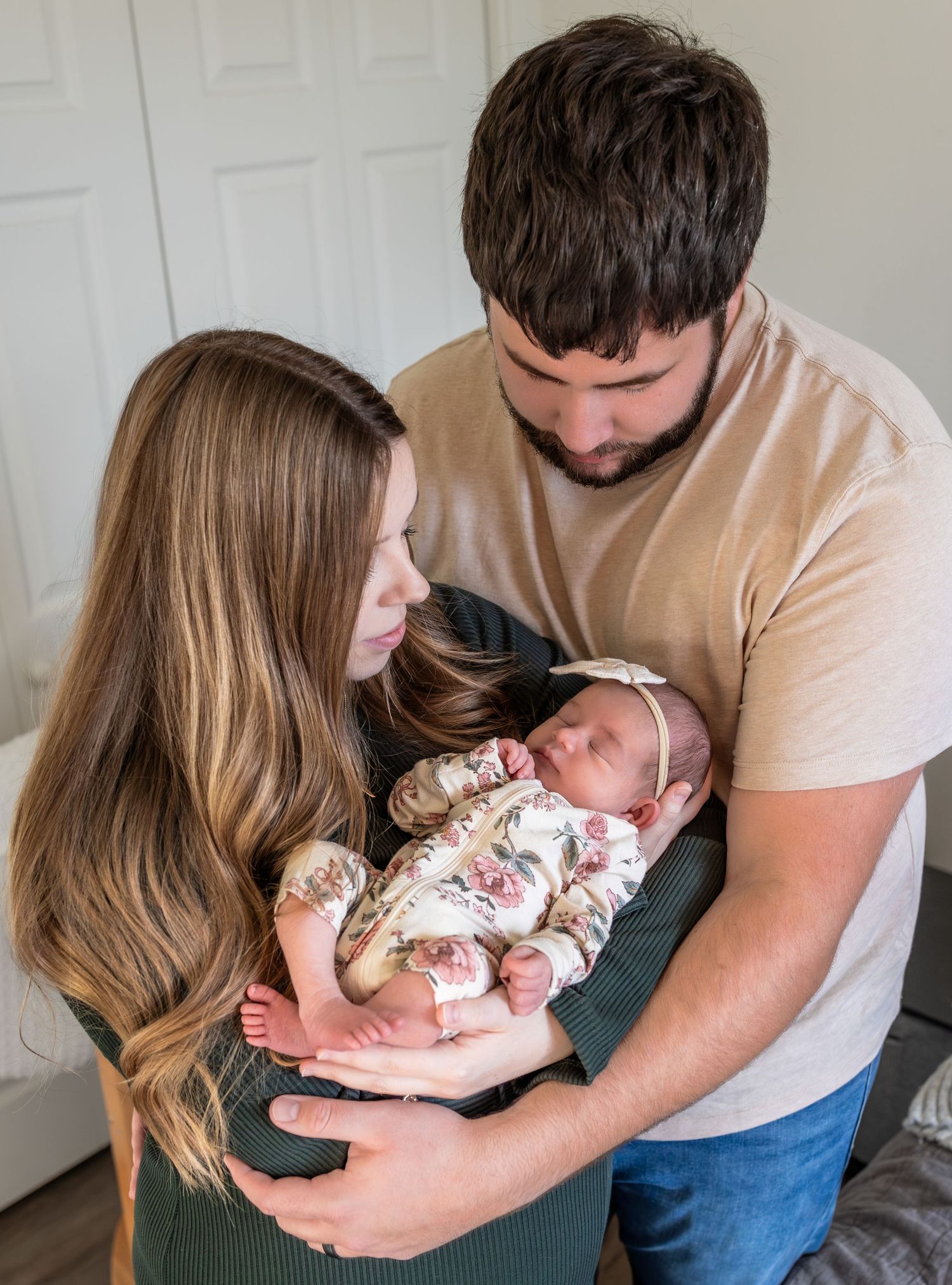 a mom and a dad look down at their newborn baby girl cradled in mom's arms.
