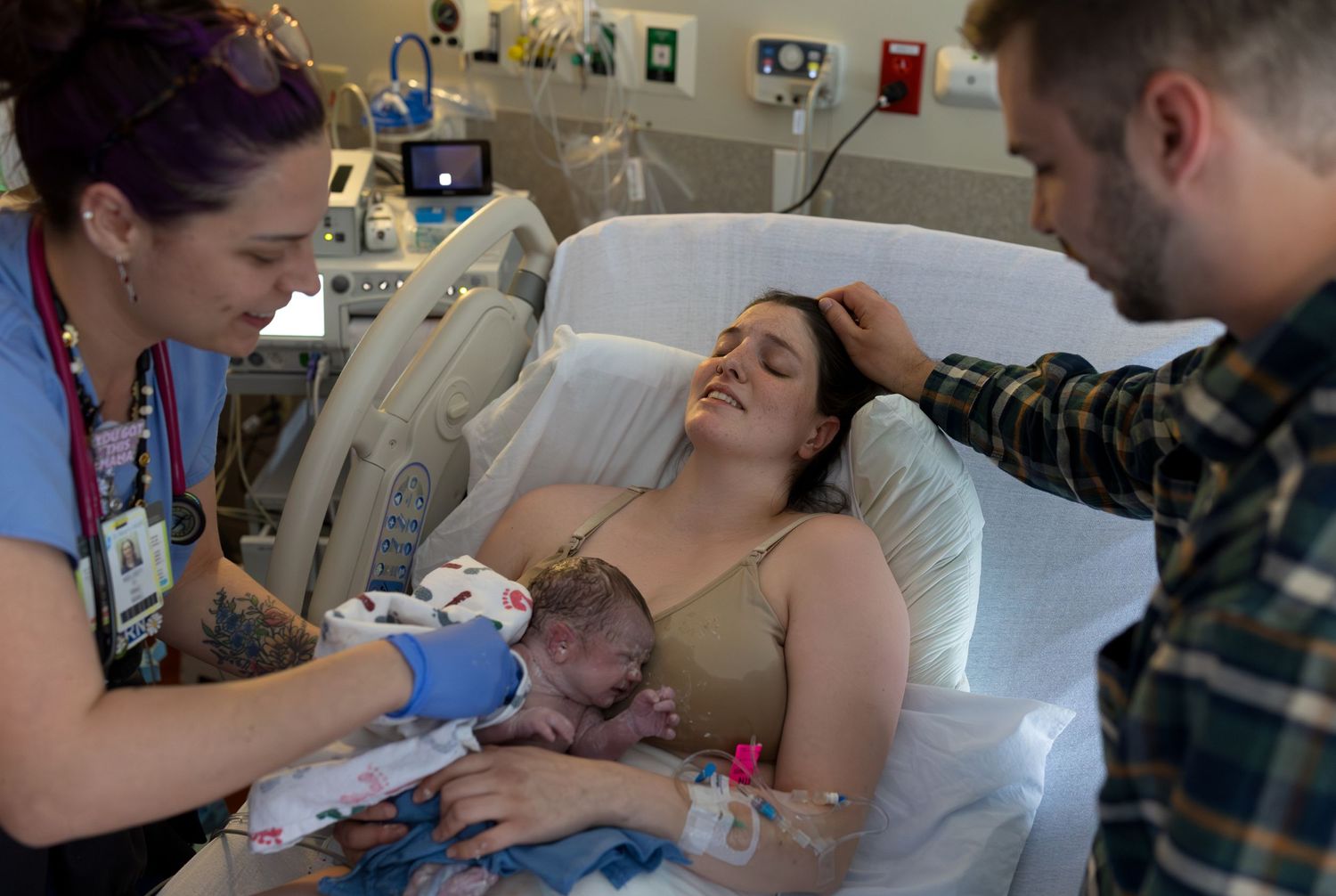 A father strokes his wife's head as she cries with joy as her newborn is laid on her chest