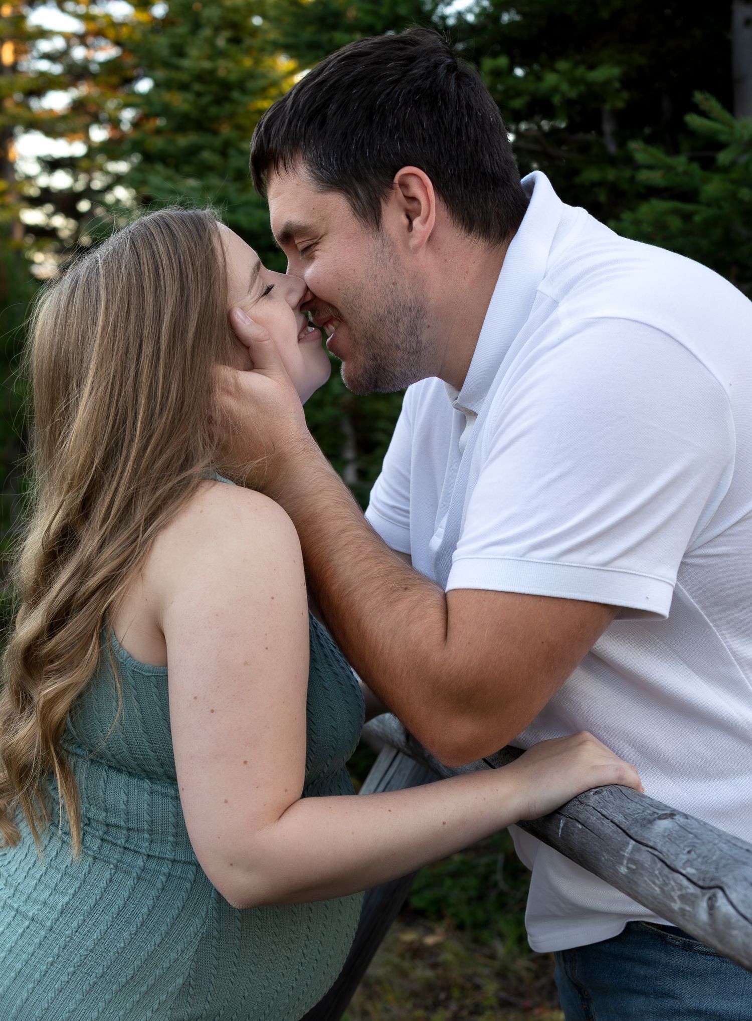 A couple lean in for a kiss in a wooded forest
