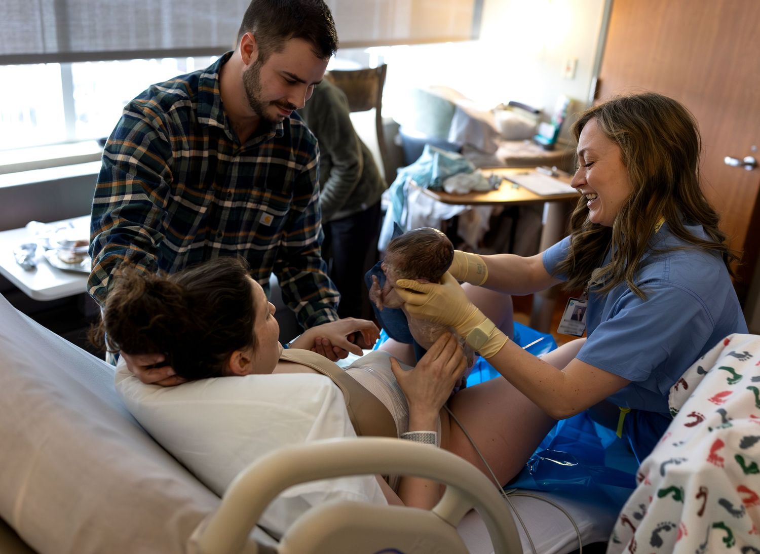 An obgyn hands a mother her newborn baby seconds after birth as the father watches over them