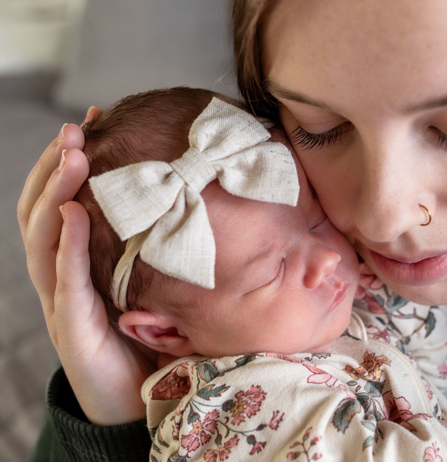 A close up image of a baby girls face with her mom's cheek pressed against the baby's cheek.