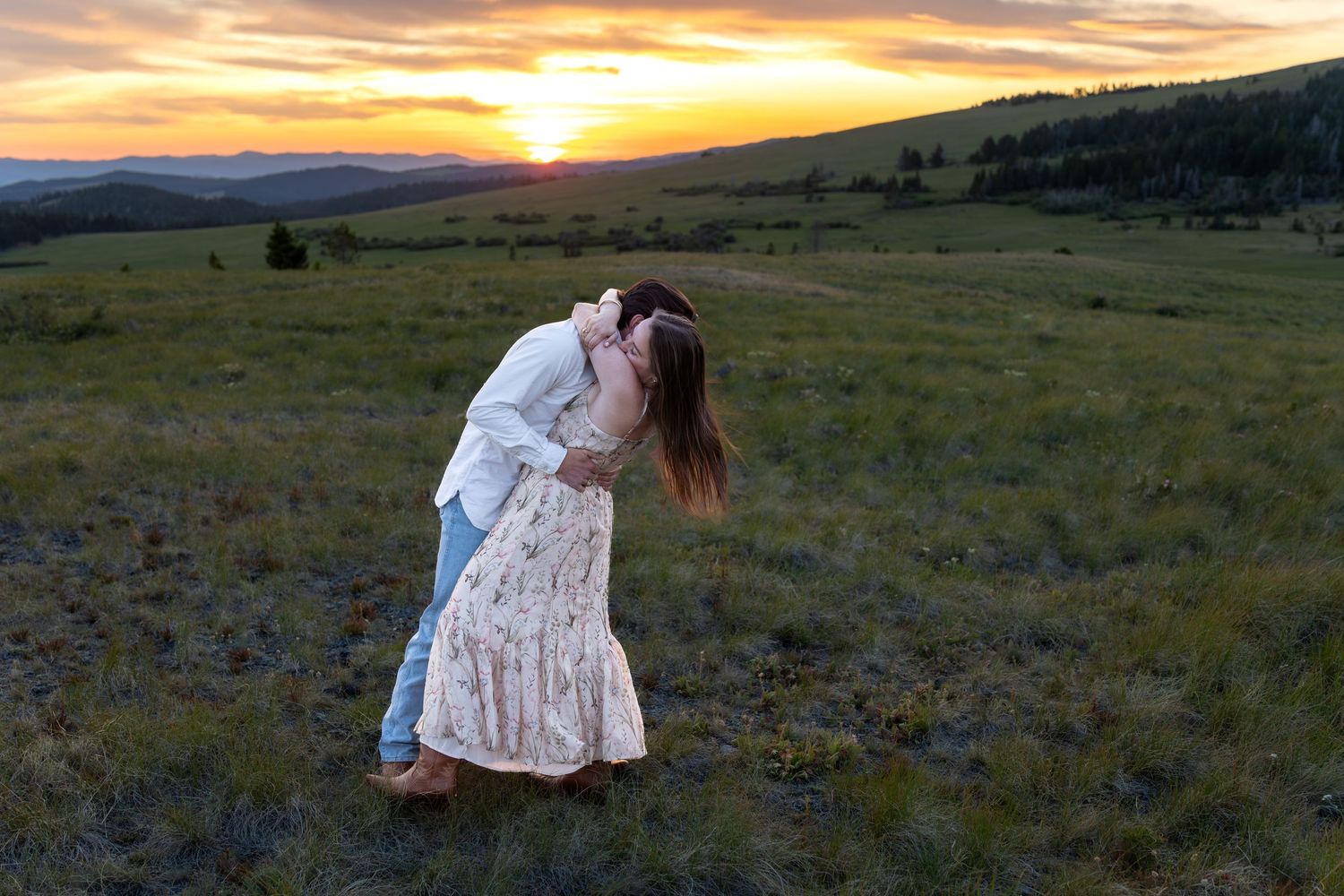 A newly engaged couple embraces on a mountain top at sunset.