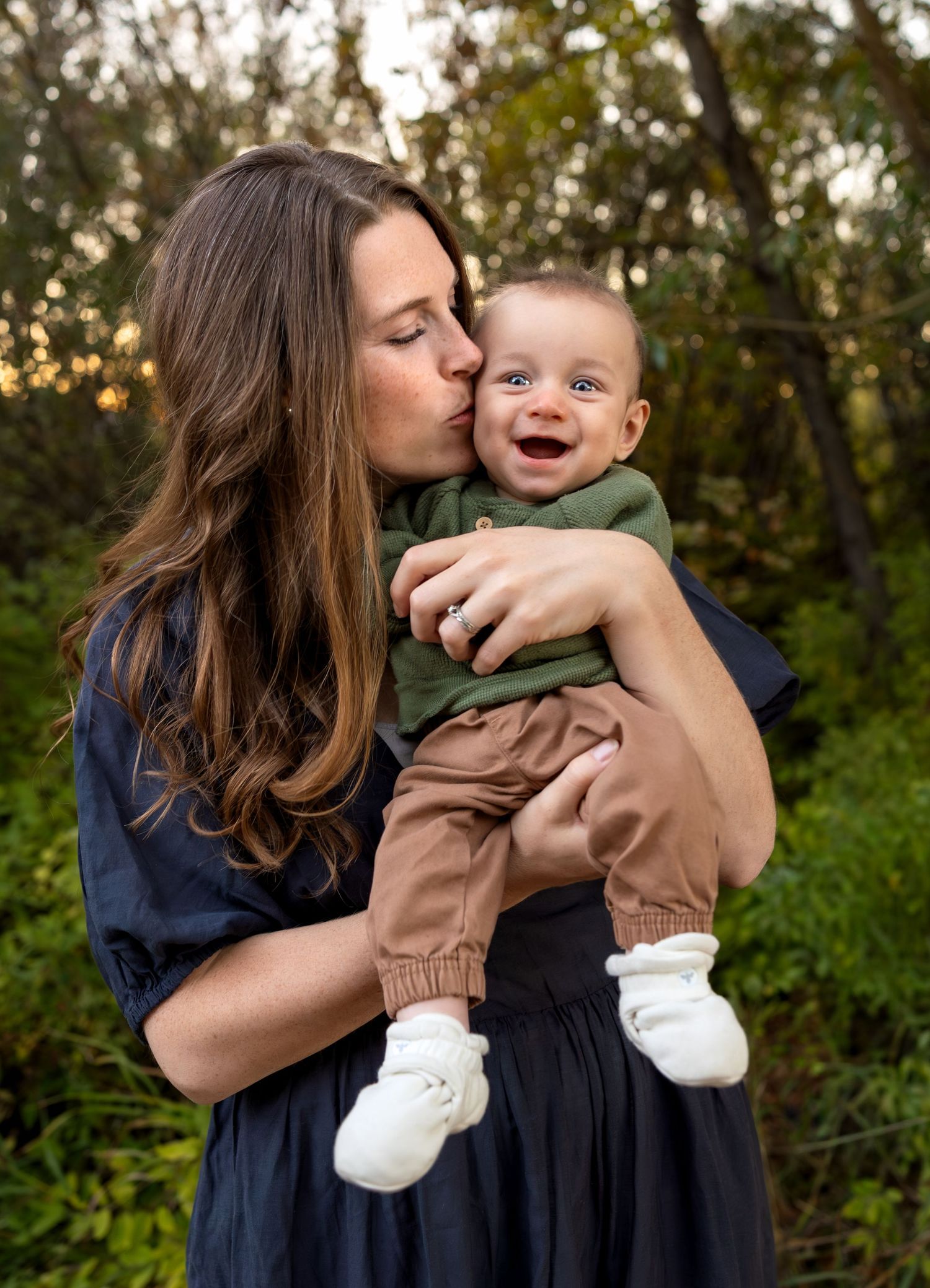 A mother holds her infant son and kisses his cheek