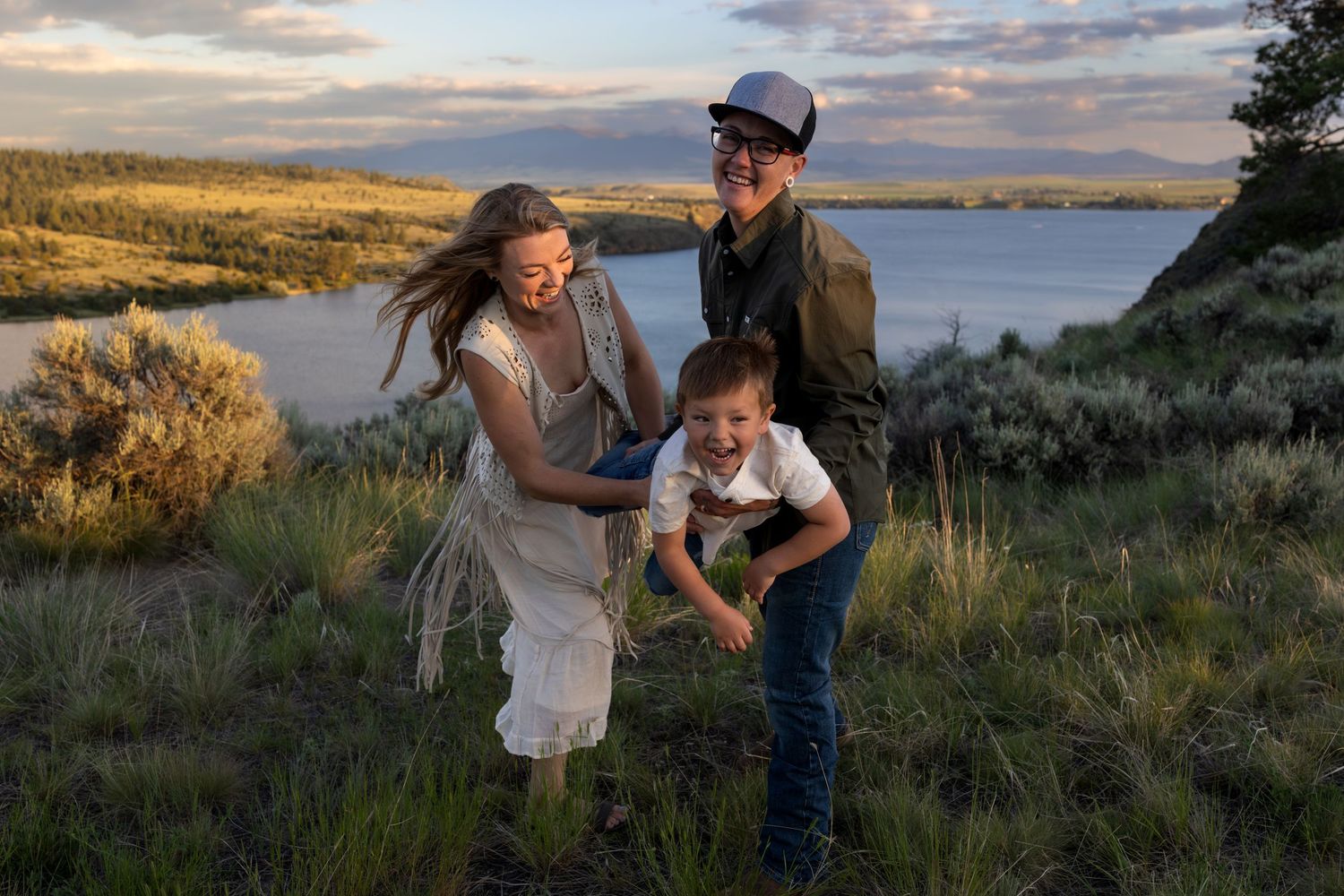 Family portrait with parents swinging young boy with lake in the background.