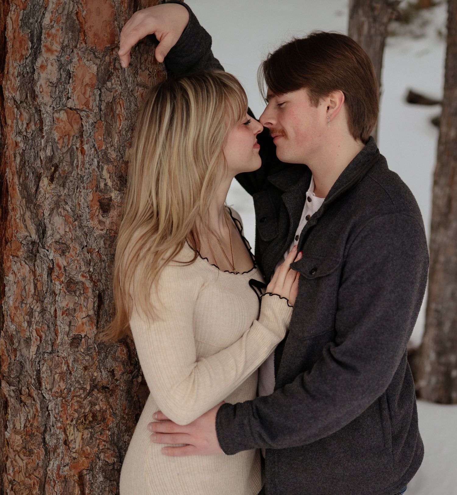 Couples engagement photo, about to kiss, leaning against a tree.