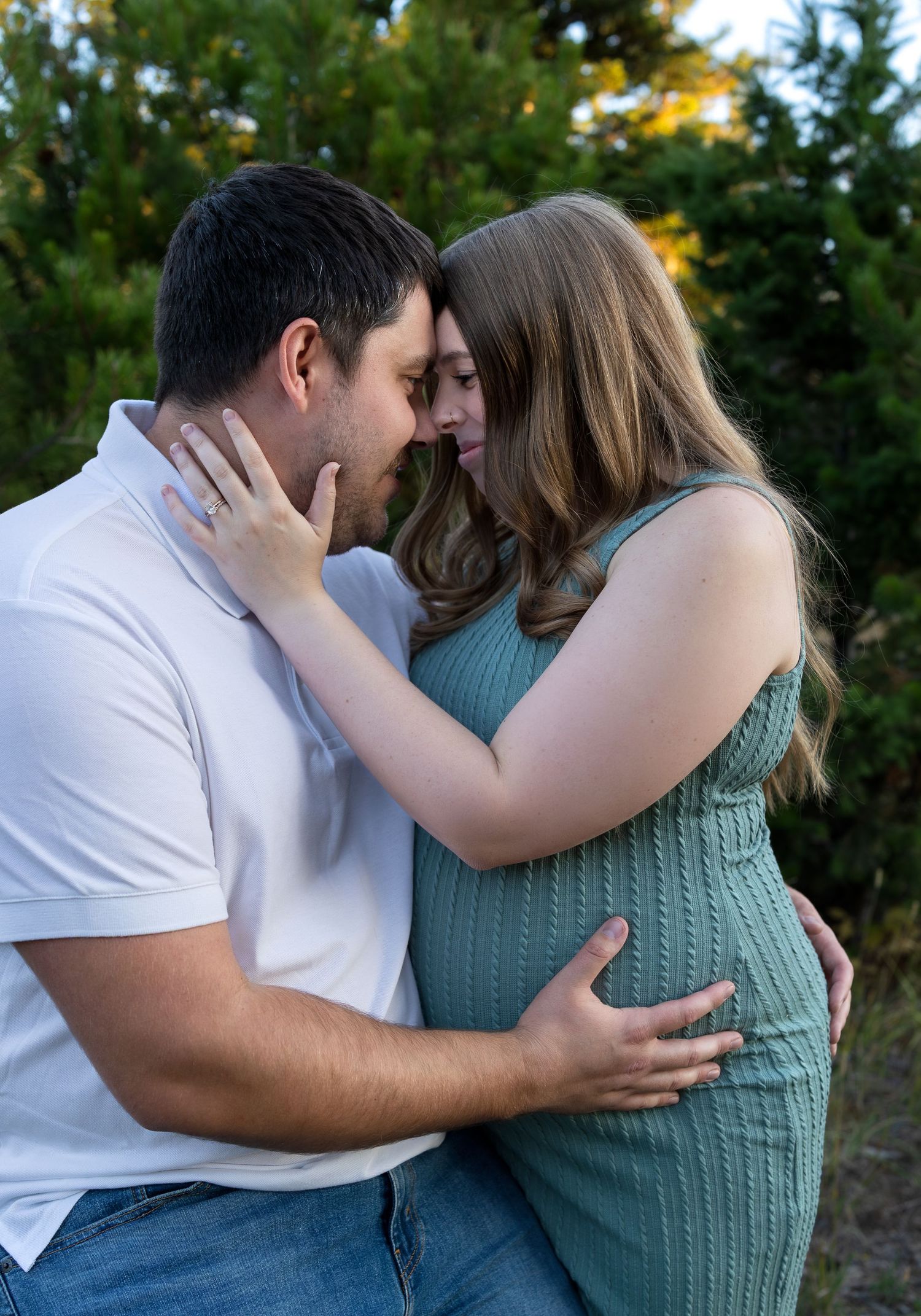 A pregnant woman and her husband touch foreheads in a tender maternity photo