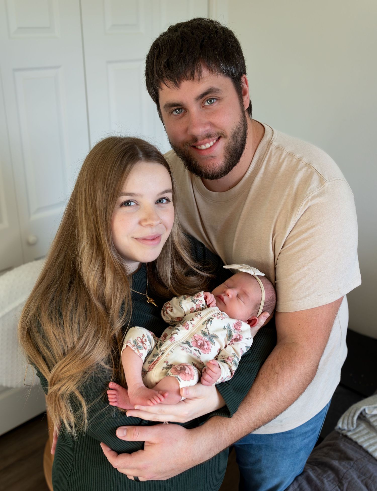 A mom and a dad smile at the camera while the mom holds her newborn baby girl.