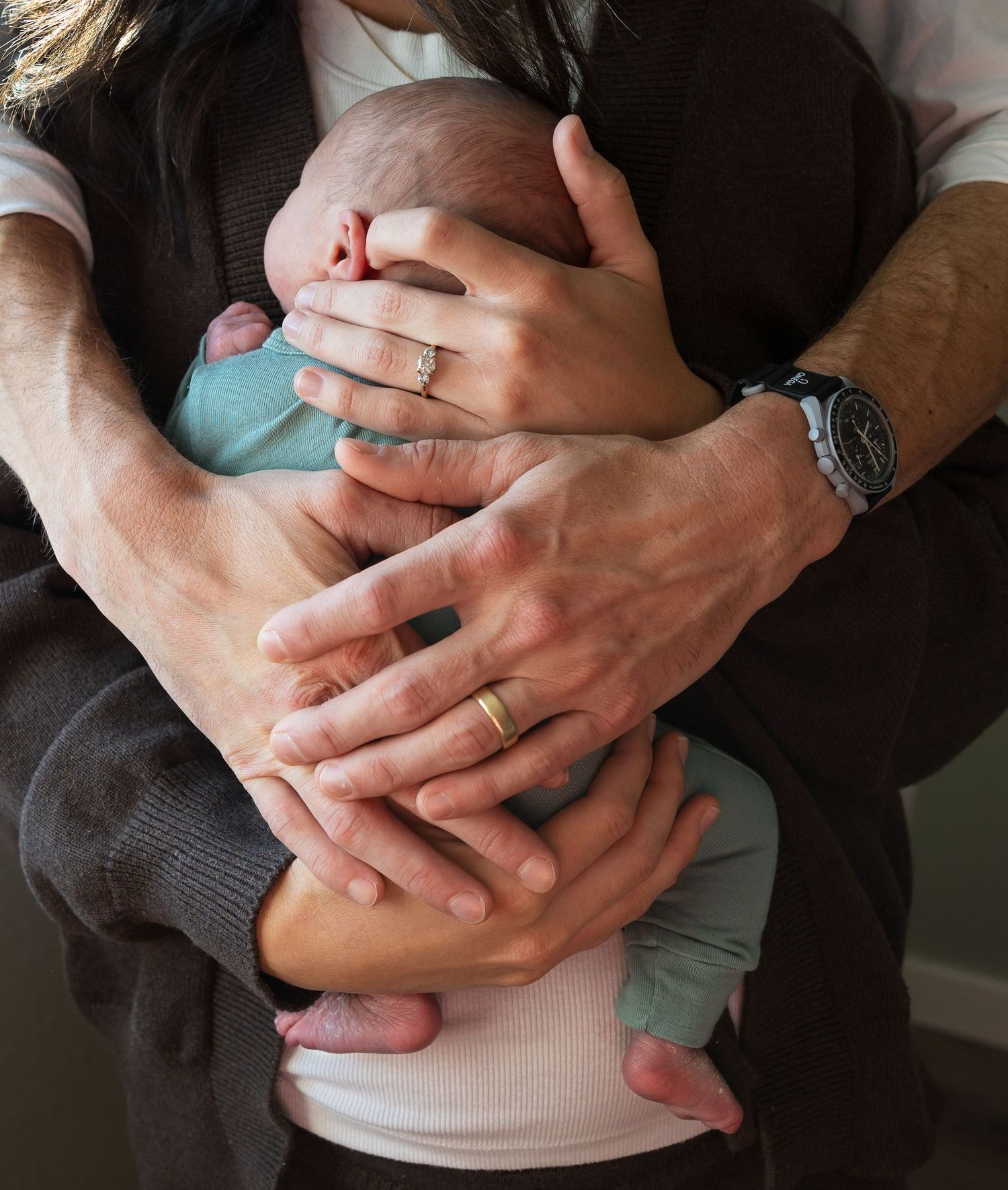 A mother and fathers hands wrapped around their newborn son