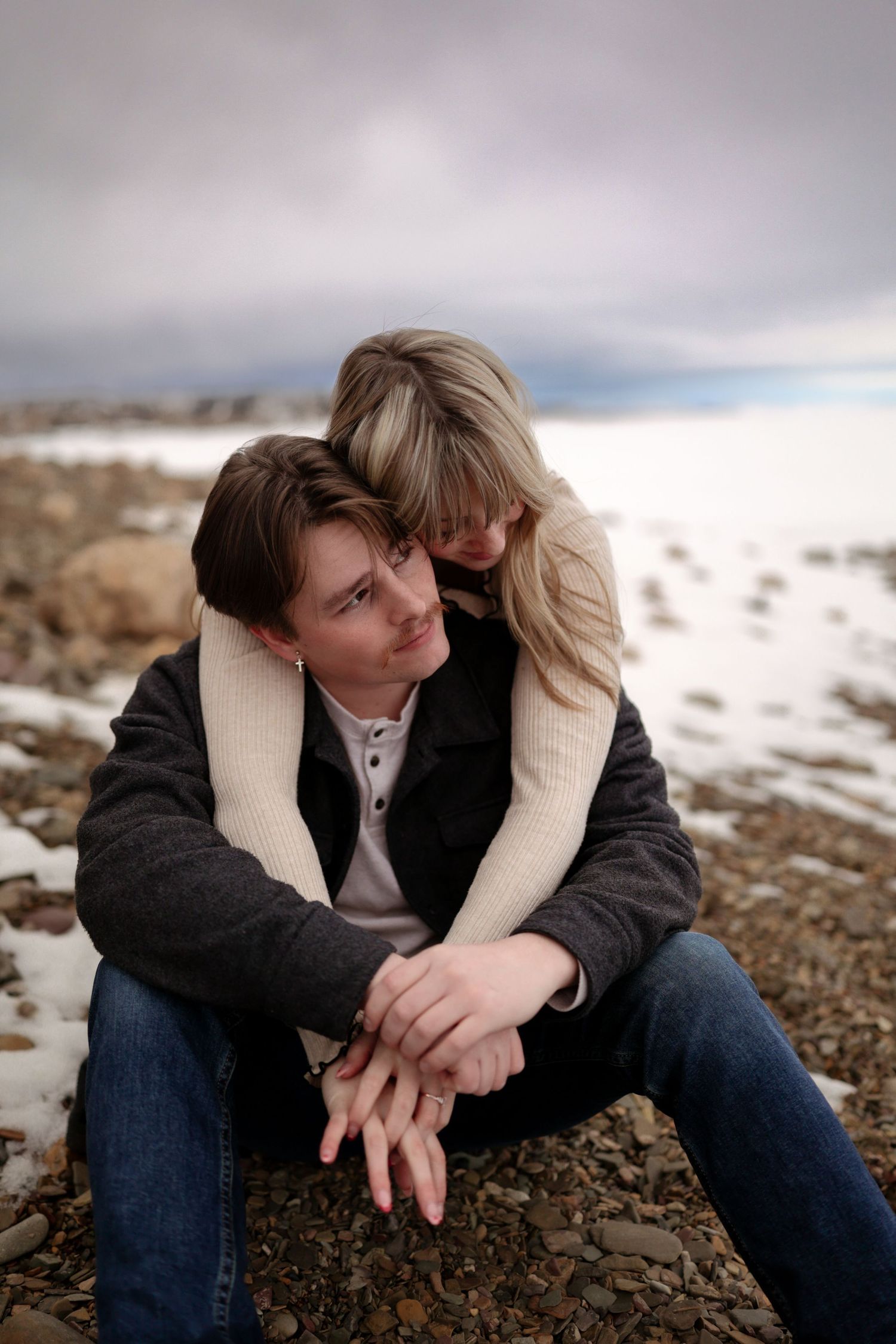 Couples engagement photo with rocky beach and lake in the background.