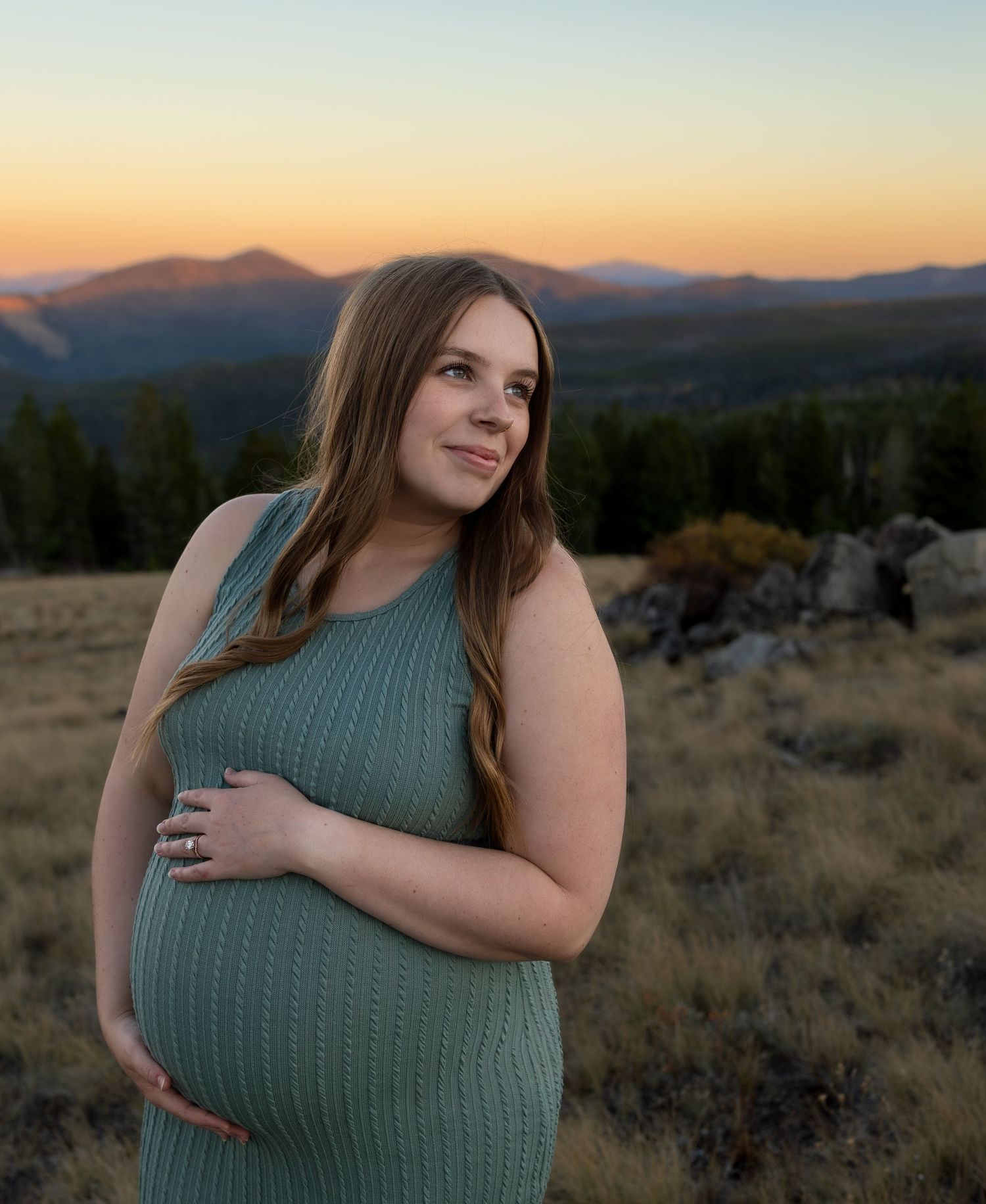 A pregnant woman holds her belly and smiles past the camera