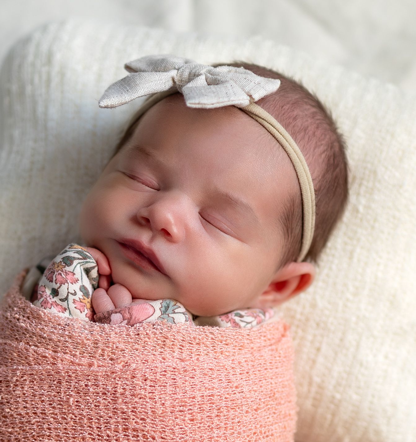 A posed up close photo of a newborn baby girl wrapped in a pink wrap.