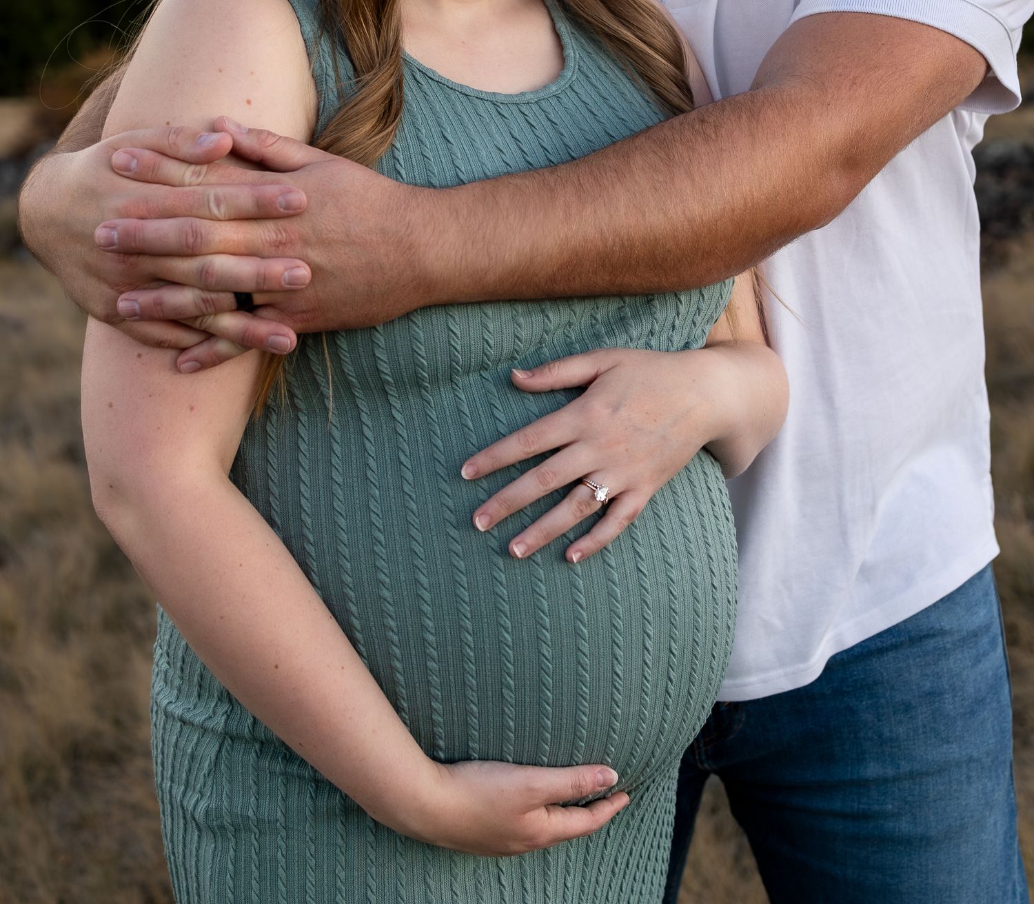 A close up of a pregnant belly with the fathers arms wrapped around the mother