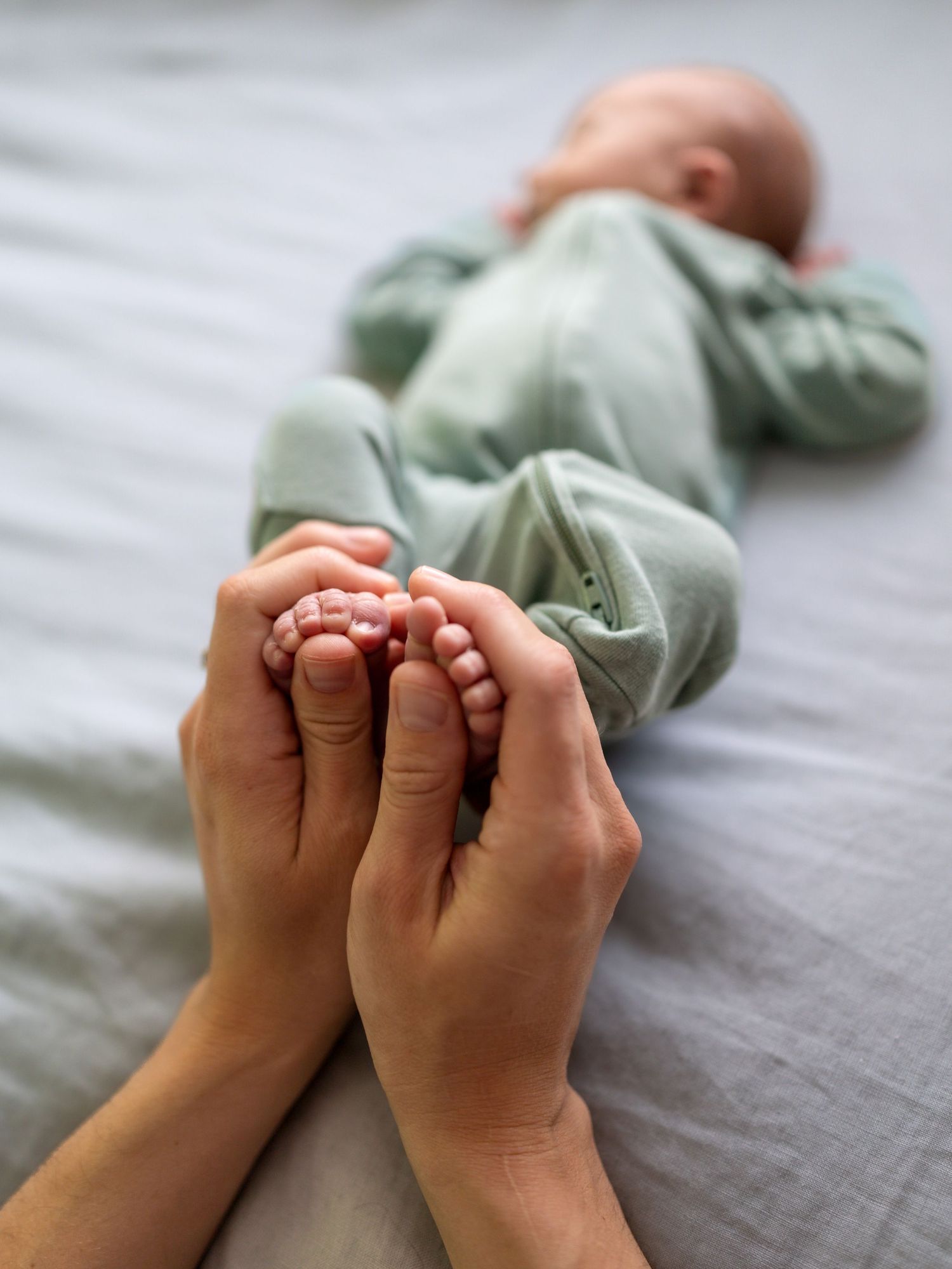 A newborn boy lays on a bed while his mothers hands hold his little feet