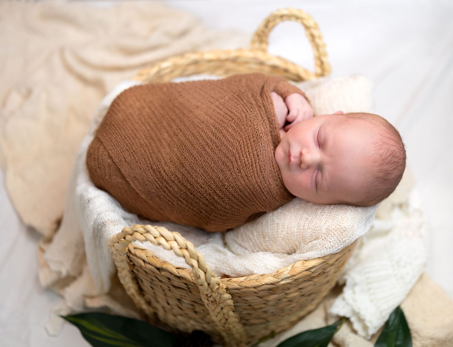 A newborn boy is wrapped in a brown wrap sleeping in a basket