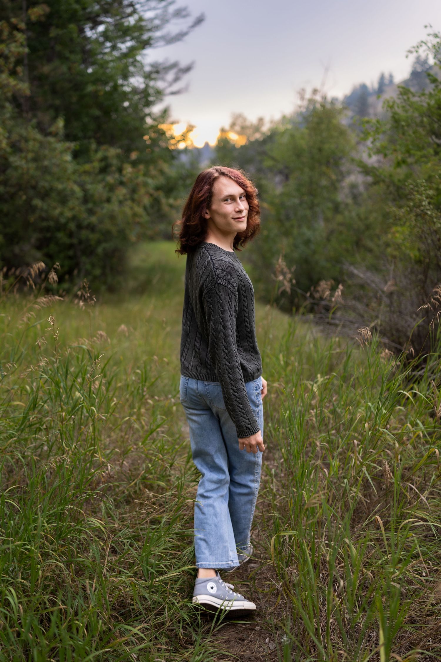 A young man walking away but turning back to smile for a photo out in the green woods