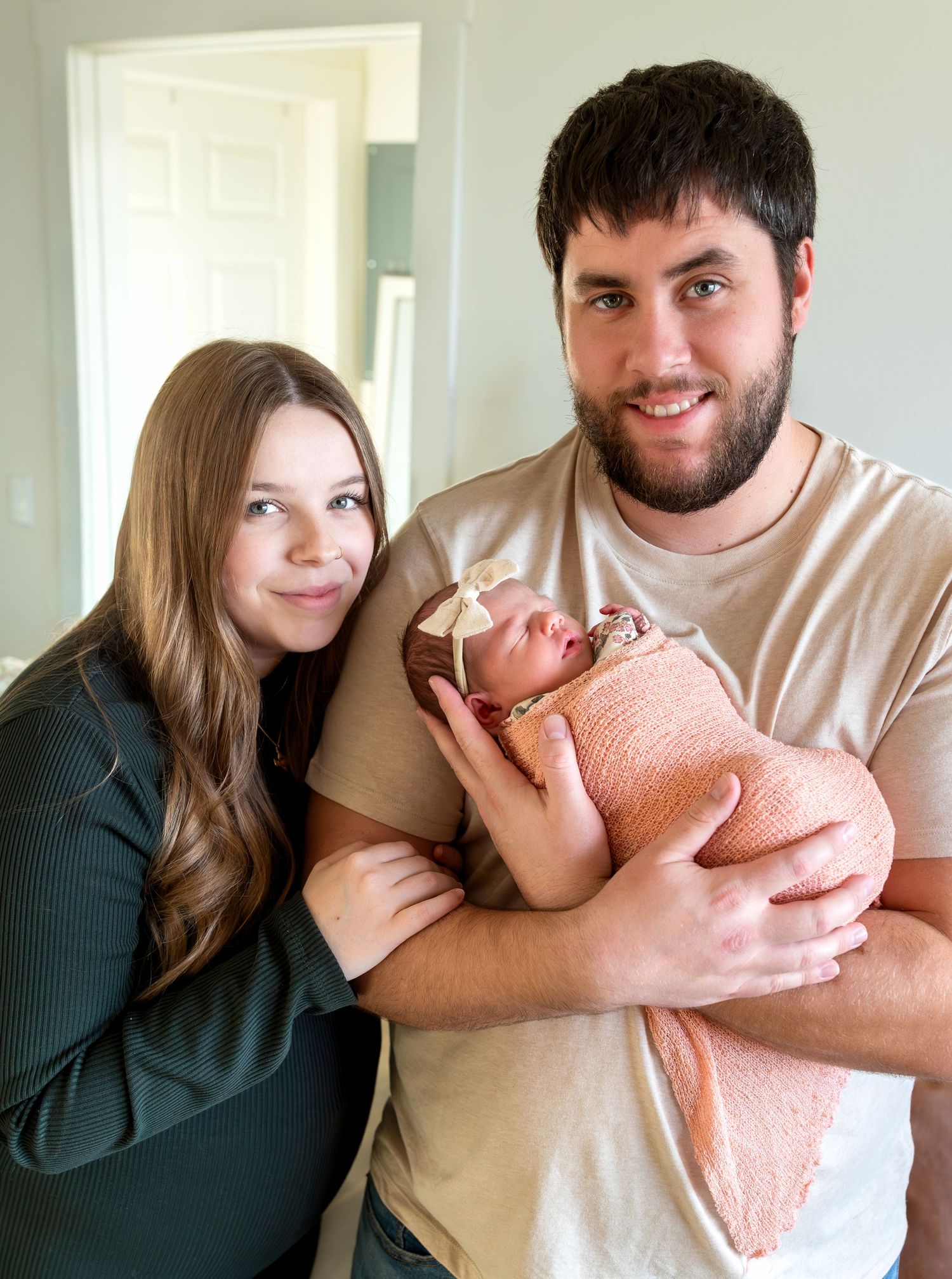 A mom and a dad smile at the camera while the dad holds his newborn baby girl.