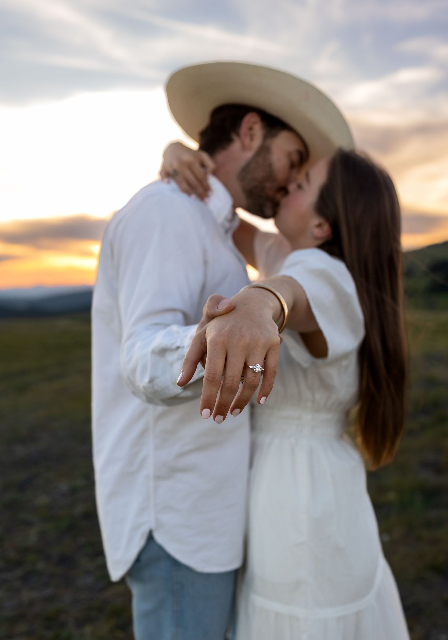 A photo of an engaged couple kissing while showing off her engagement ring.