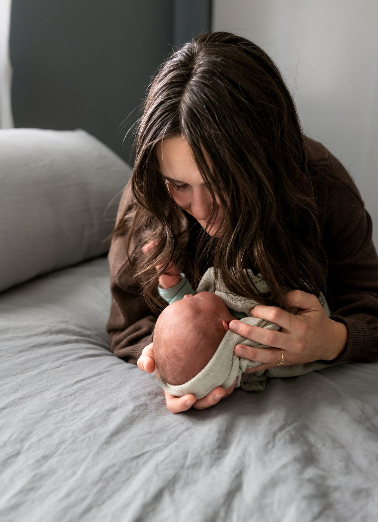 A new mother cradles her newborn on her bed in this in home newborn session.