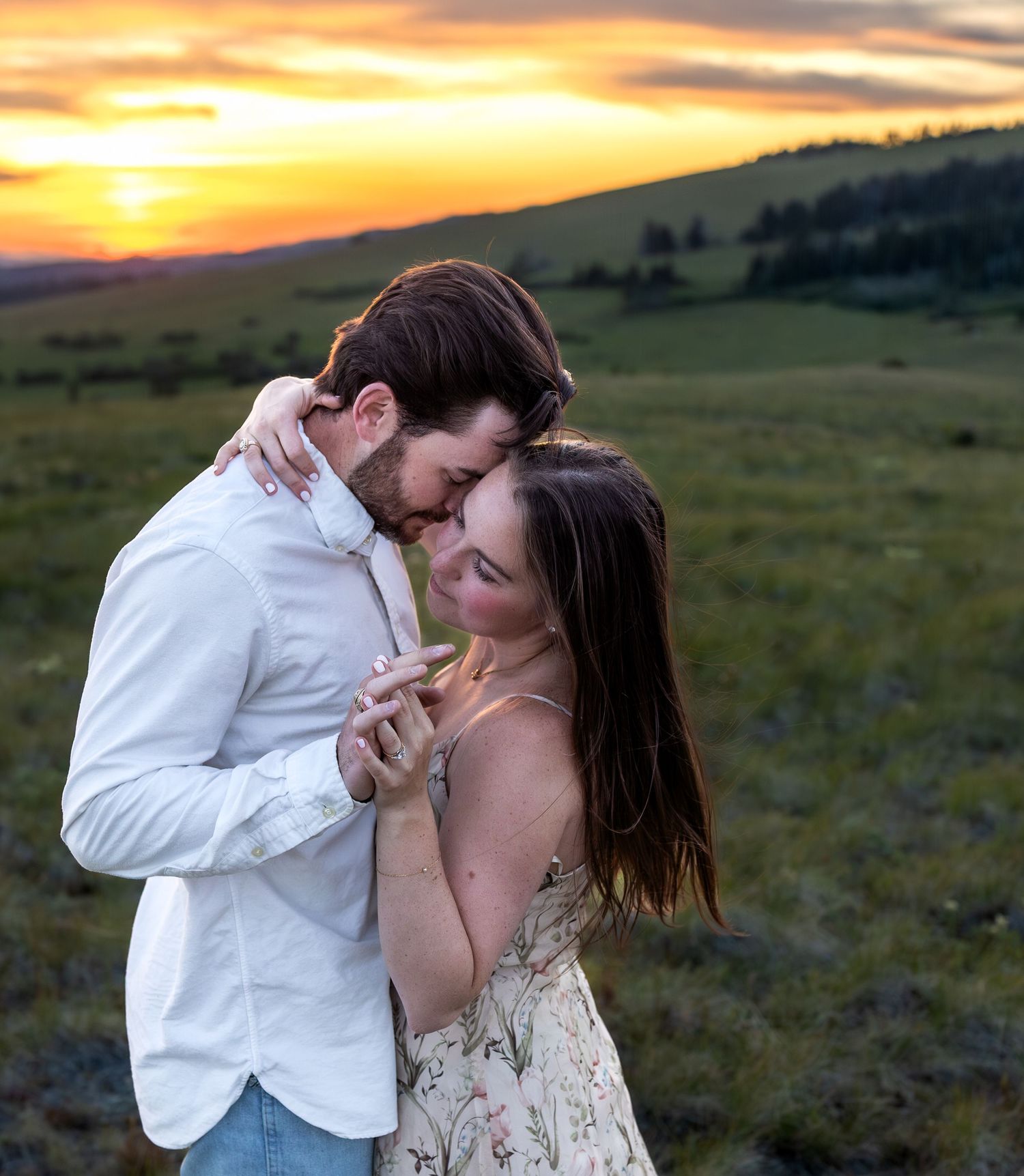 A couple embraces at the top of a mountain with the sunset behind them.