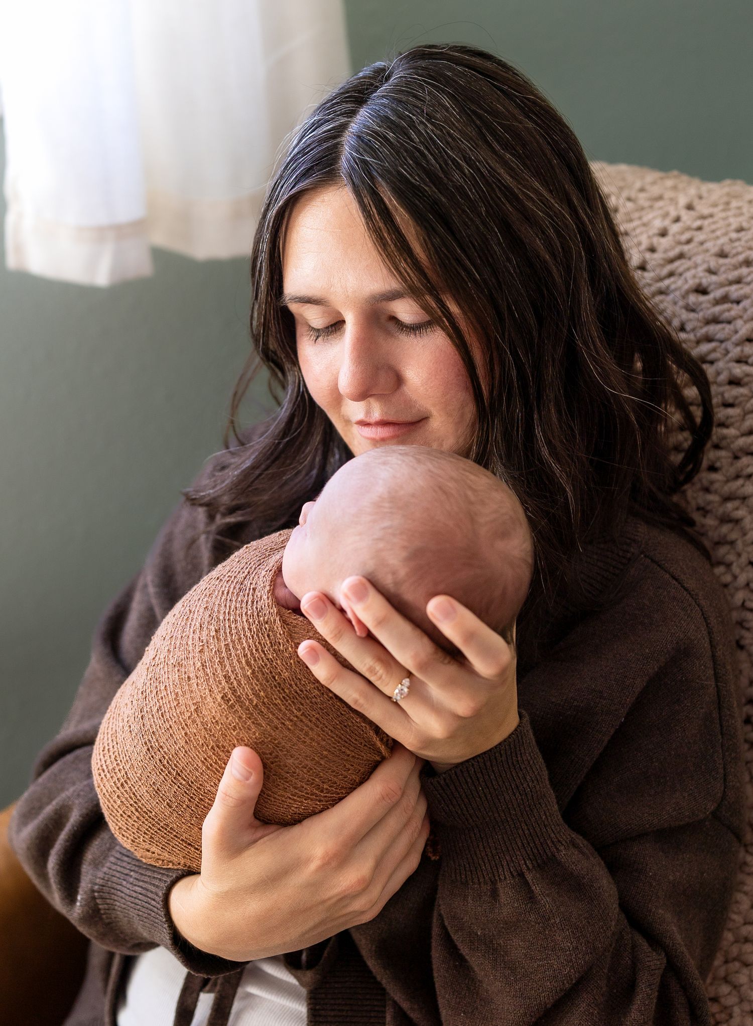 A mother sits in a rocking chair and smiles down at her newborn son