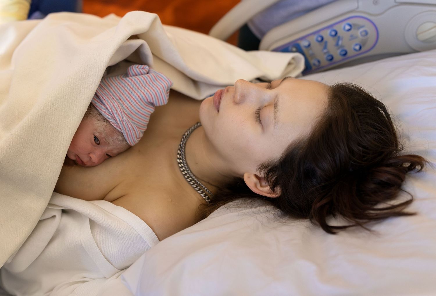 A new mother rests peacefully with her newborn baby covered by a blanket on her chest after birth
