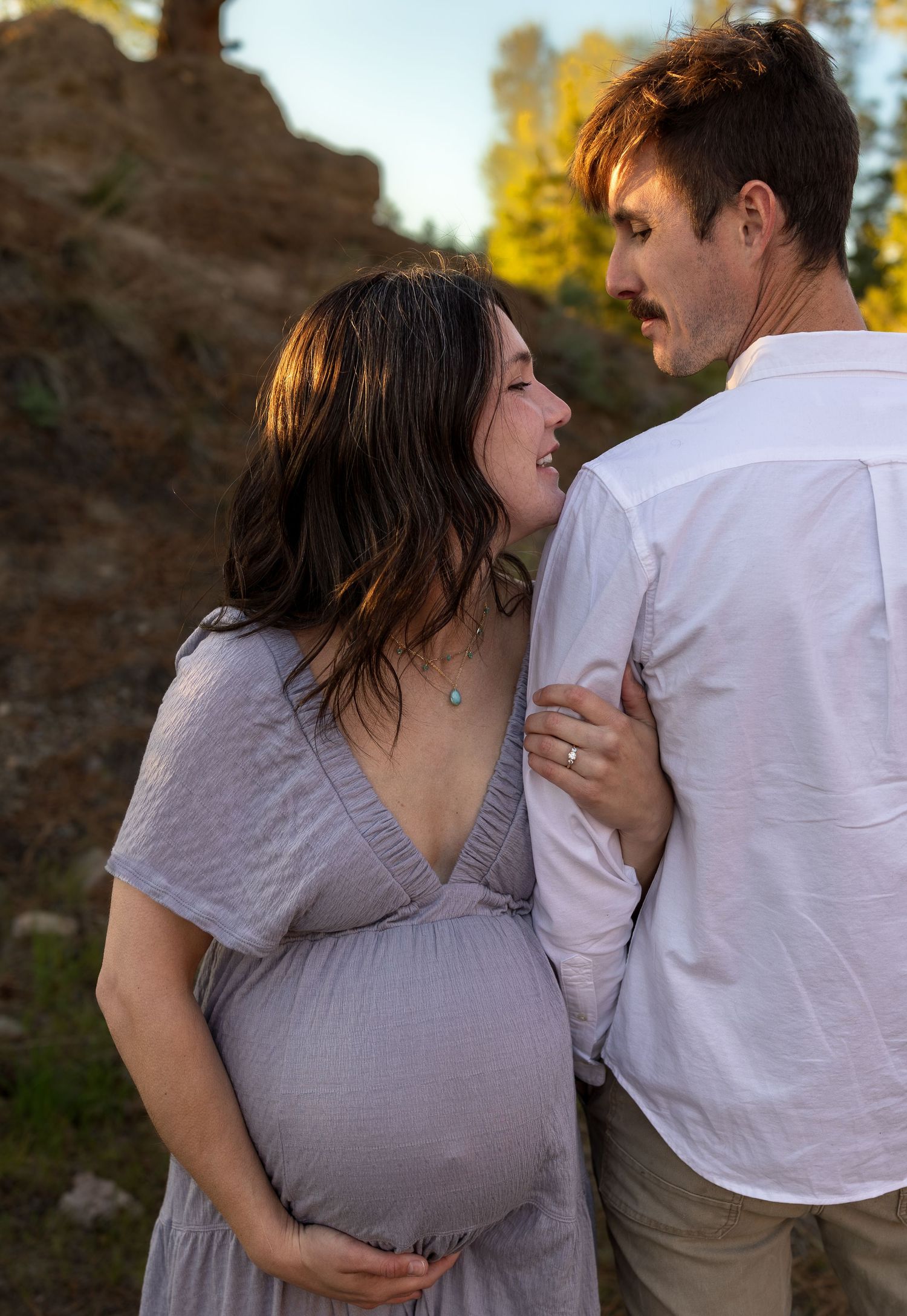A pregnant woman smiles at her husband while resting her chin on his shoulder