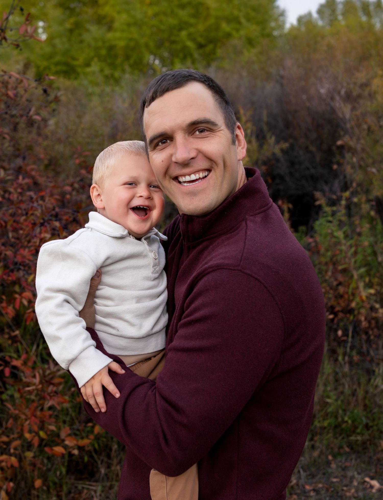 A father holds his toddler son as the smile for a photo