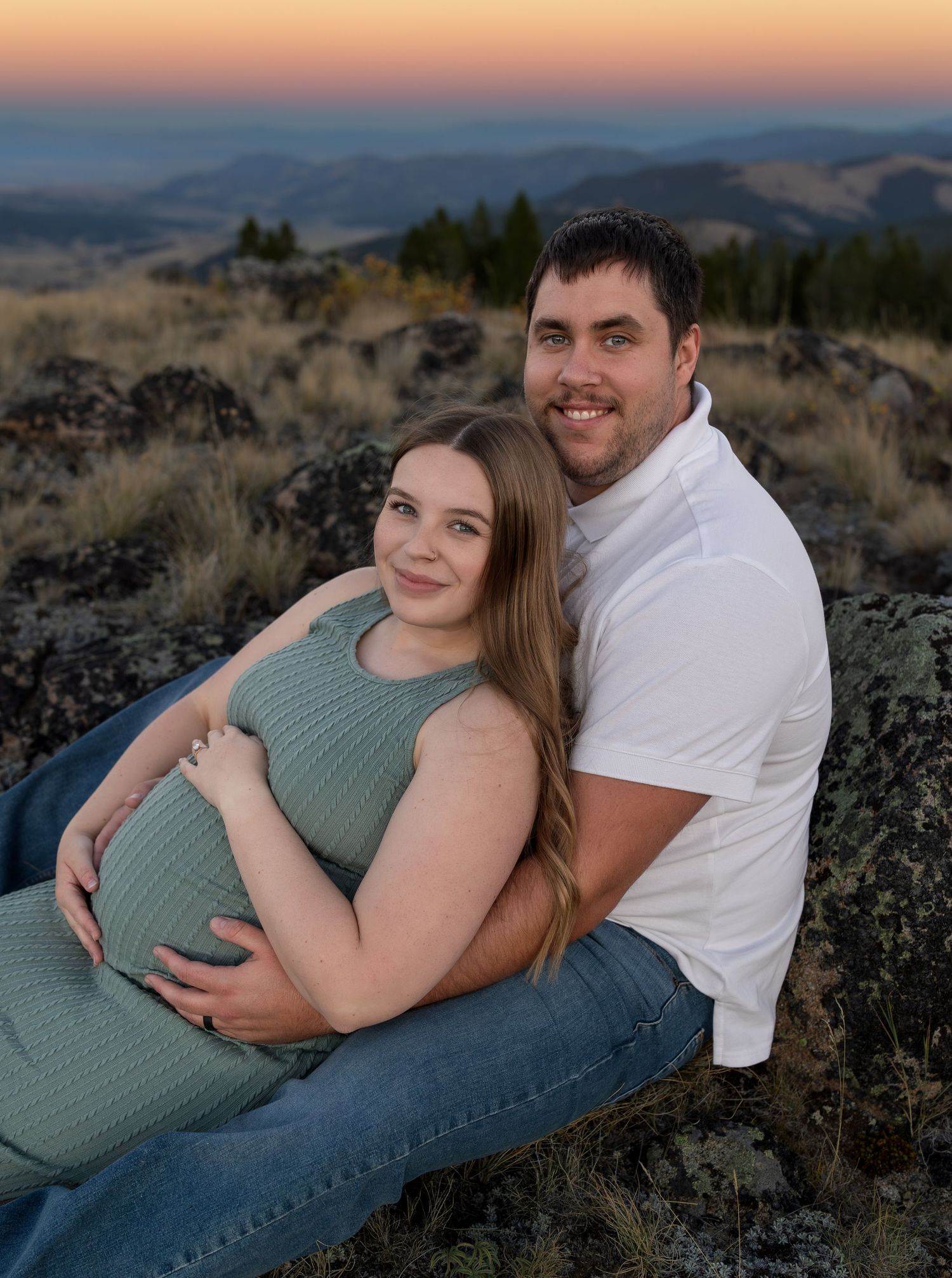 A man and pregnant woman caress her belly at sunset on a mountain