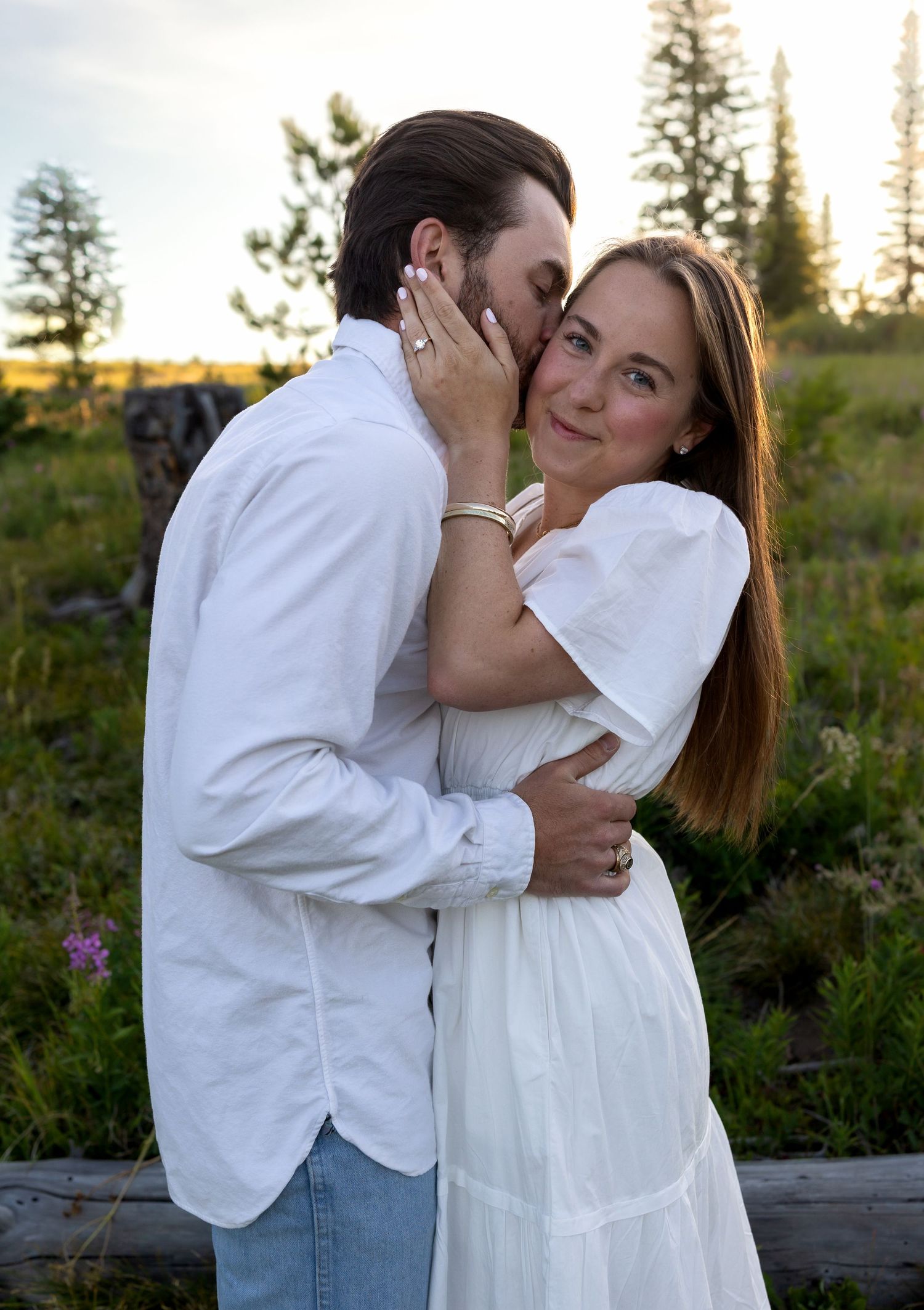 A man kisses his fiancees cheek as she rests her hand on his face and smiles at the camera