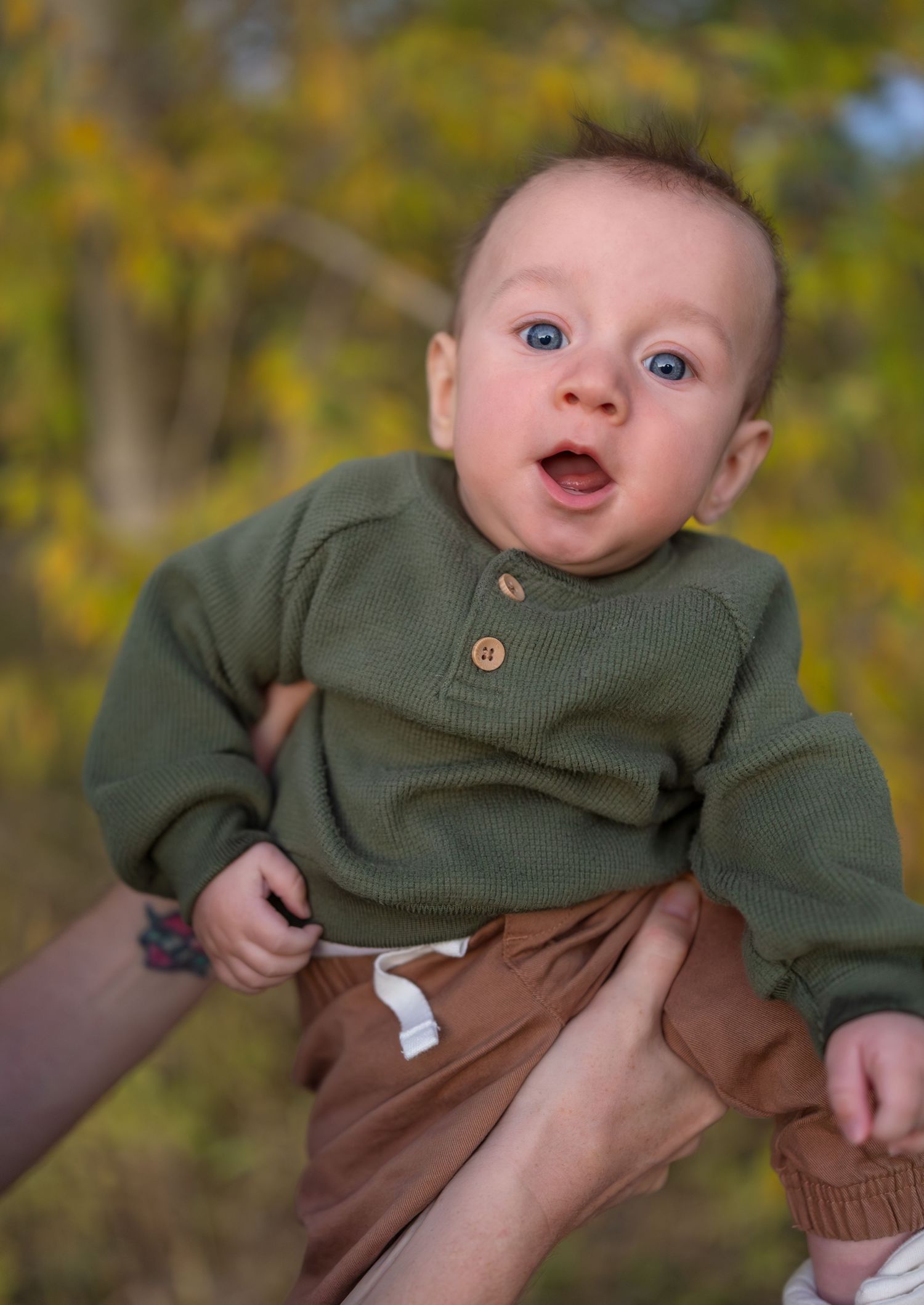 A portrait of an infant boy in front of green trees
