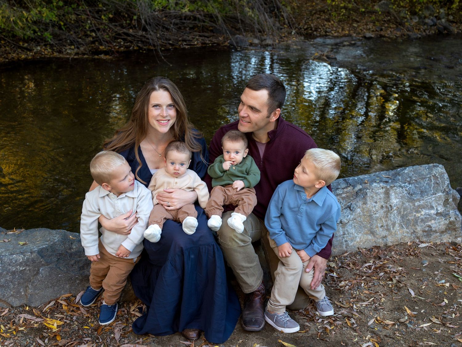 A family sits on a rock ledge in front of a river