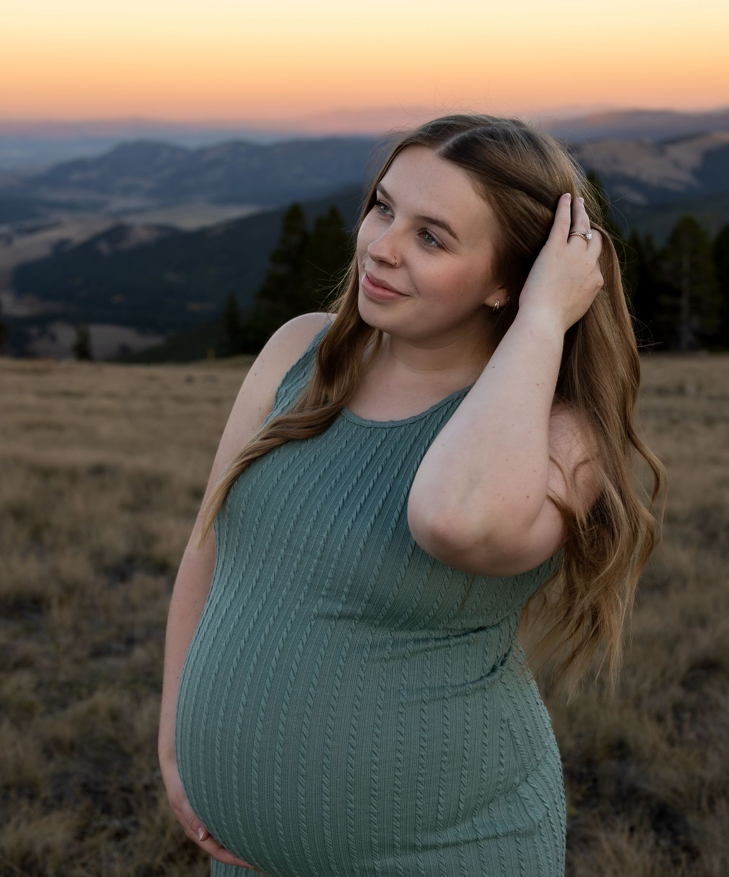 A pregnant woman poses on top of a mountain