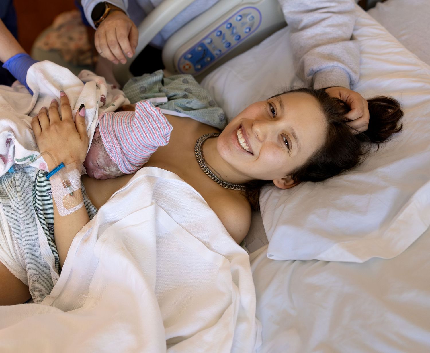 A new mom smiles at the camera with her newborn baby on her chest moments after birth