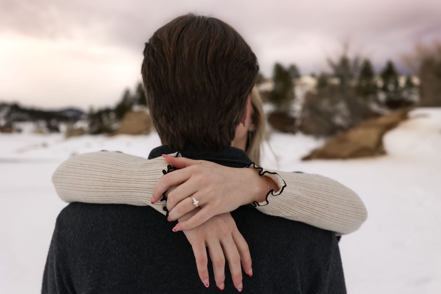 A close up of an engagement ring as the woman's arms are wrapped around her fiancé's neck