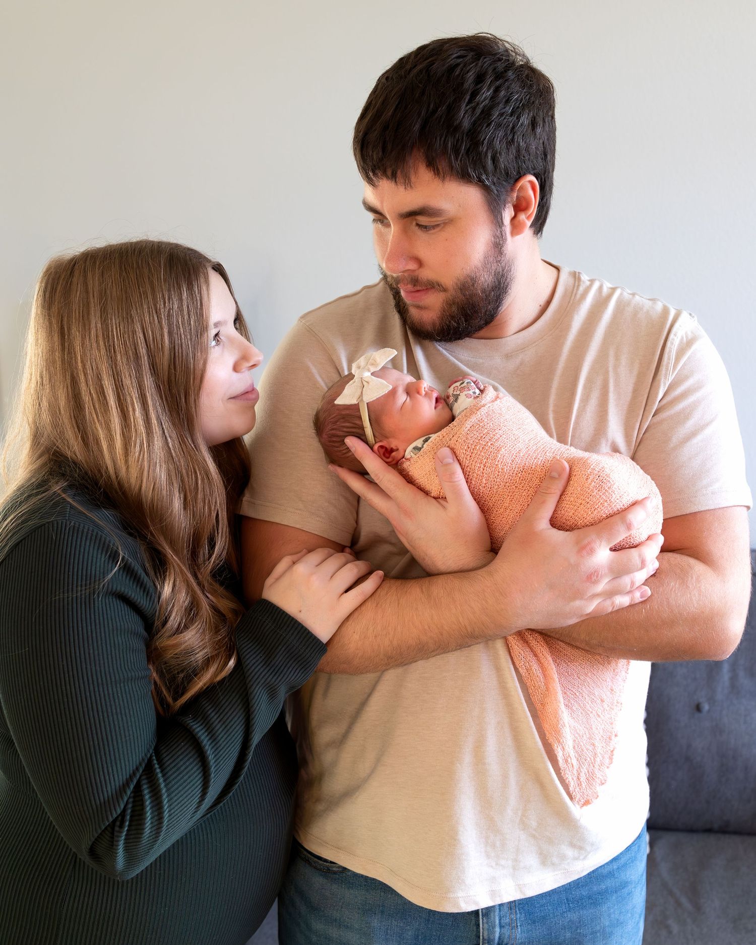 A mom and dad smile at each other with their newborn baby girl cradled in Dad'd arms.