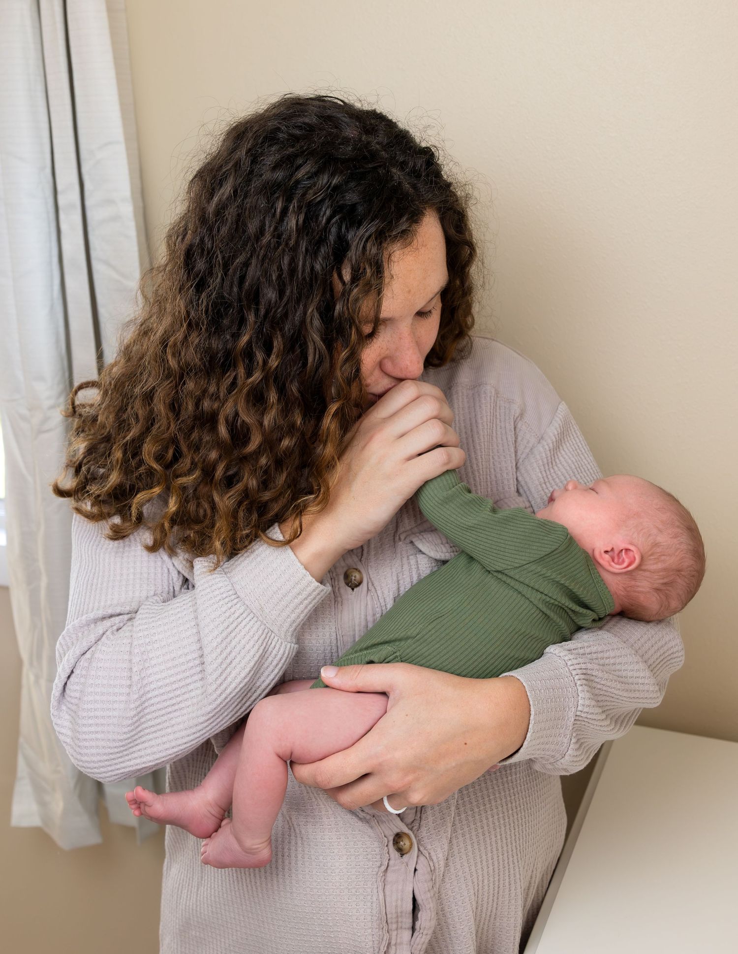 A new Mother holds her newborn son as she kisses his tiny hand.