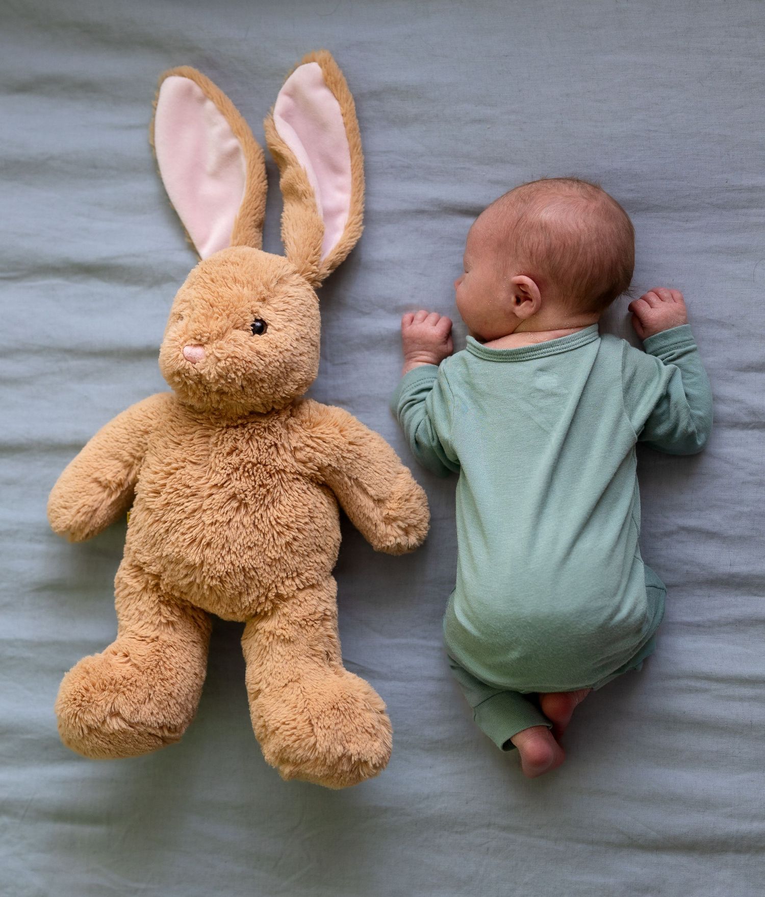 A newborn boy lays scrunched up on his tummy next to a stuffed bunny