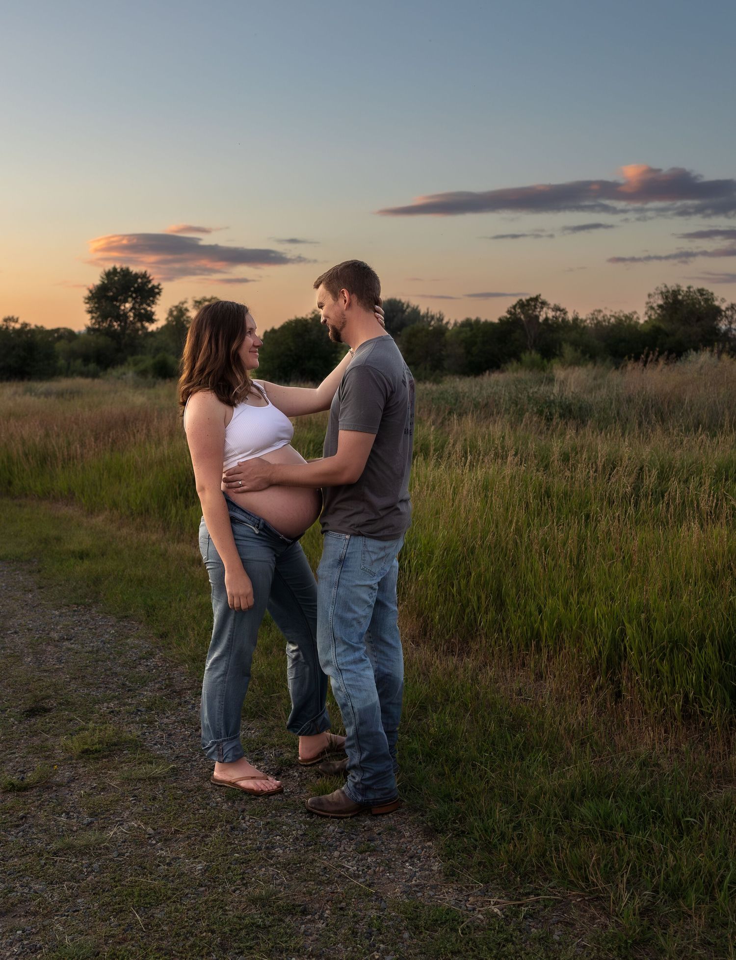 A pregnant woman and her husband share a moment in the middle of a country field at sunset