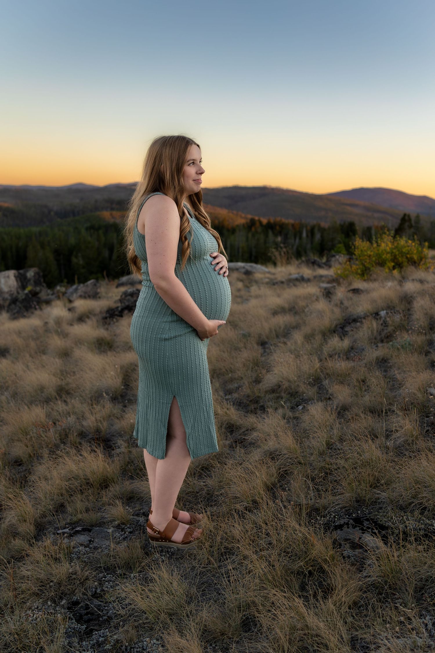 A pregnant woman poses with her baby bump on a mountain