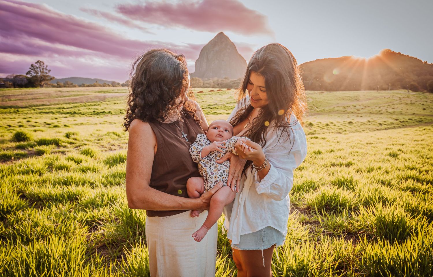 Family enjoying a tender moment in a scenic field at sunset with mountain backdrop.