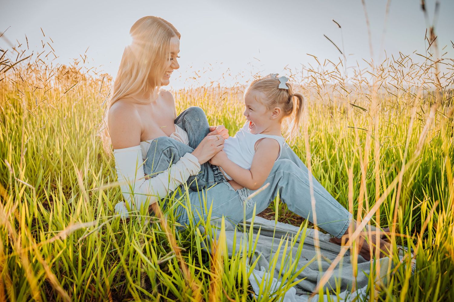 Tender moment shared between adult and child sitting together in tall golden grass at sunset.
