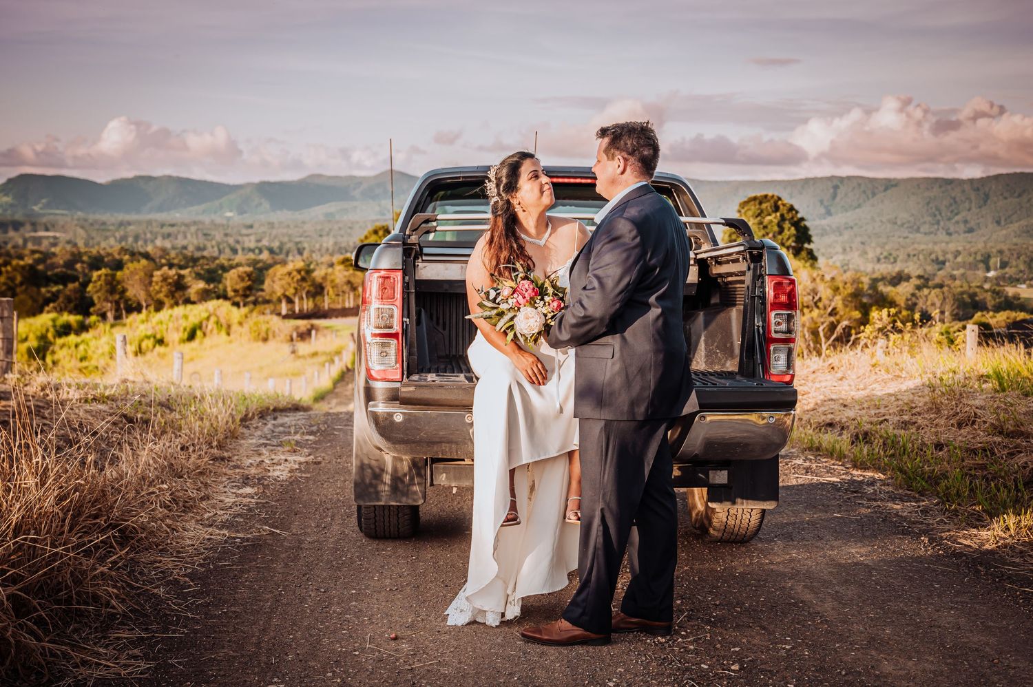 Couple sharing romantic moment by pickup truck on country road with mountain views.
